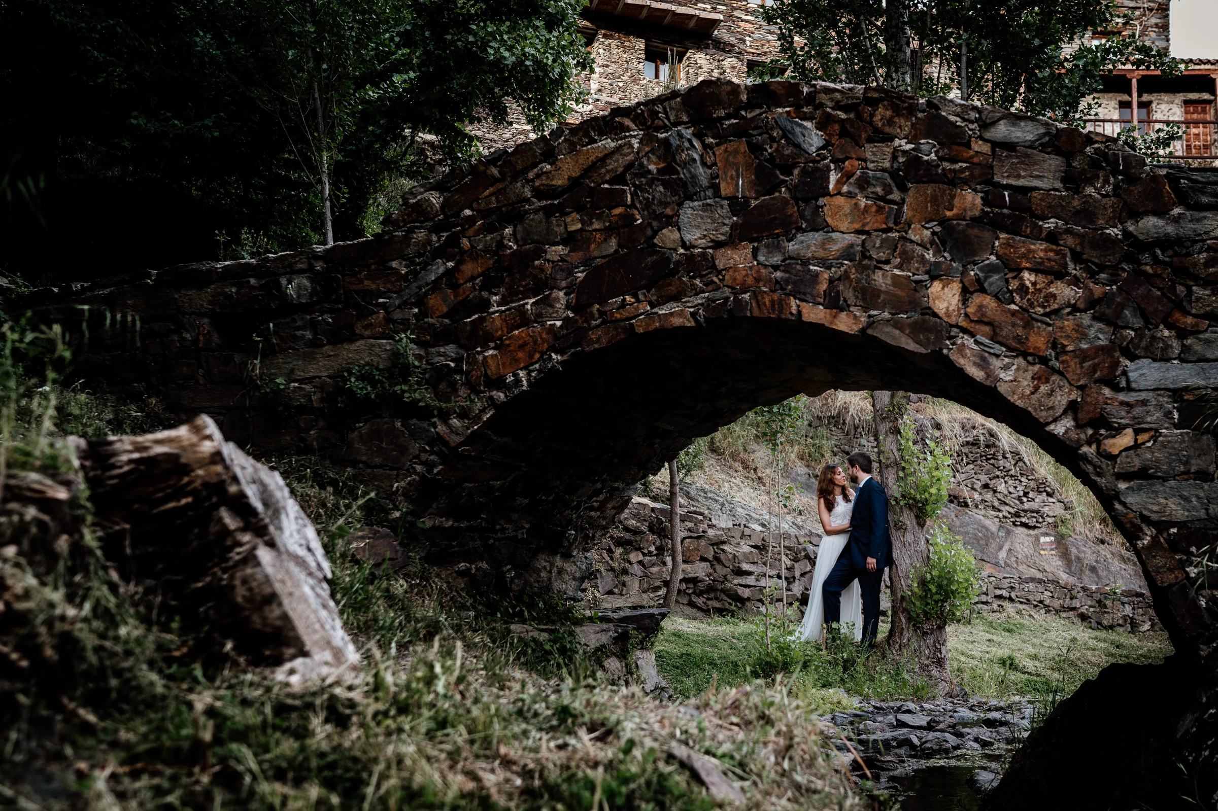 Ainhoa y Fer, retrato amplio de la pareja bajo un puente tradicional de piedra, Madrid