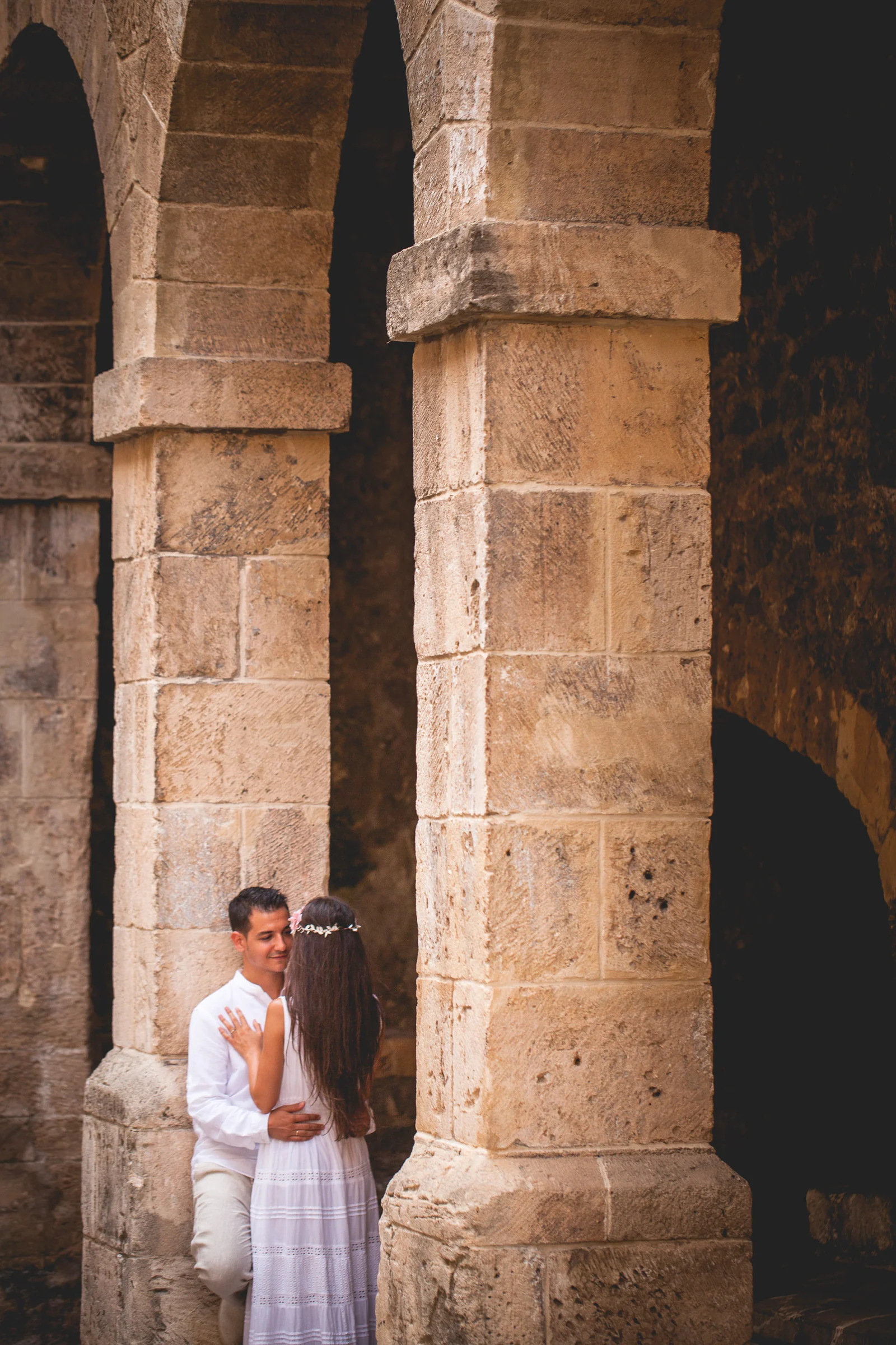 Retrato vertical de Alba y Jorge entre columnas de piedra, postboda de Alba y Jorge en Ibiza fotografiada por Pedro Zamorano.
