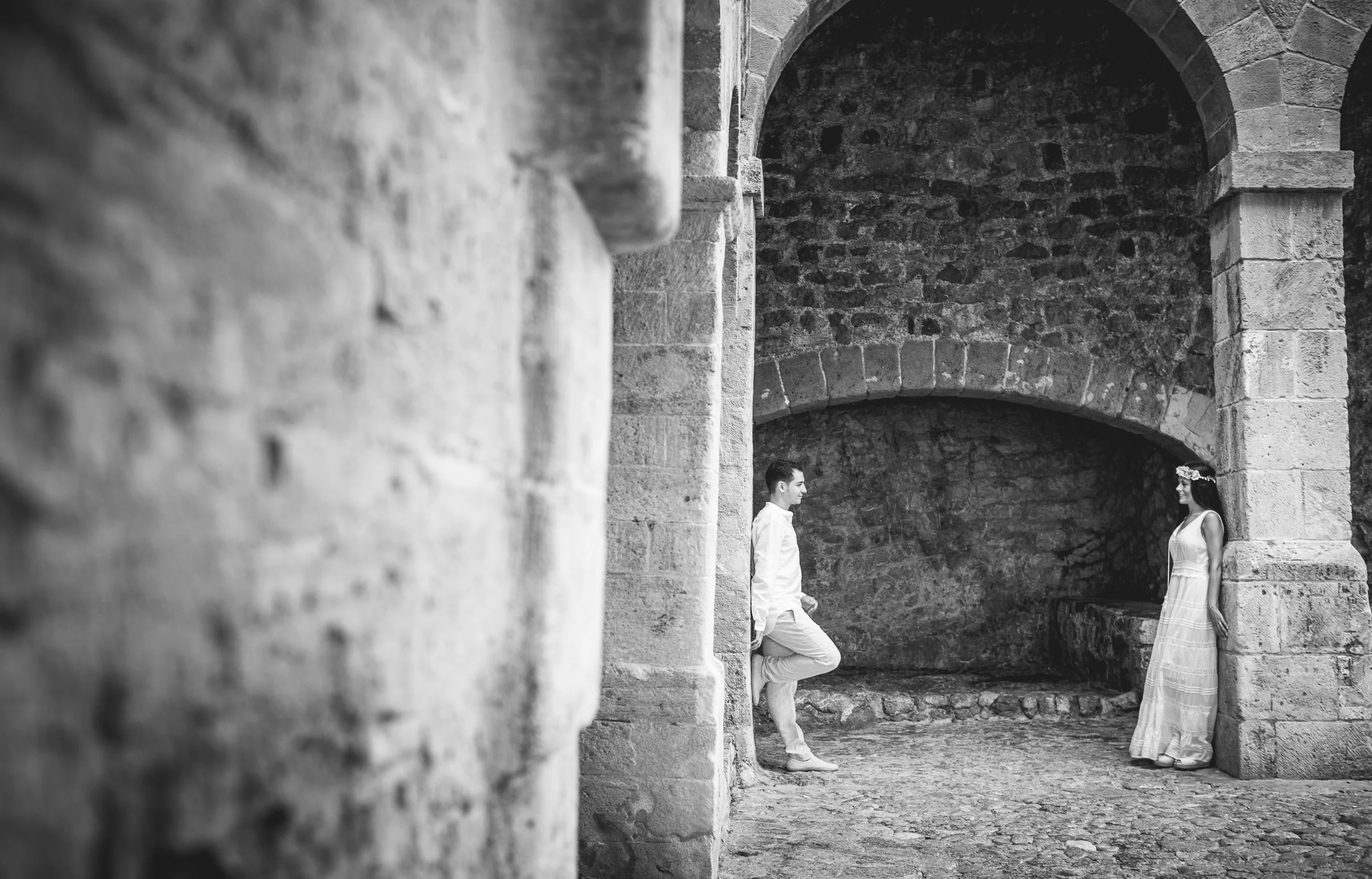 Alba y Jorge separados por un arco de piedra en blanco y negro, postboda de Alba y Jorge en Ibiza fotografiada por Pedro Zamorano.