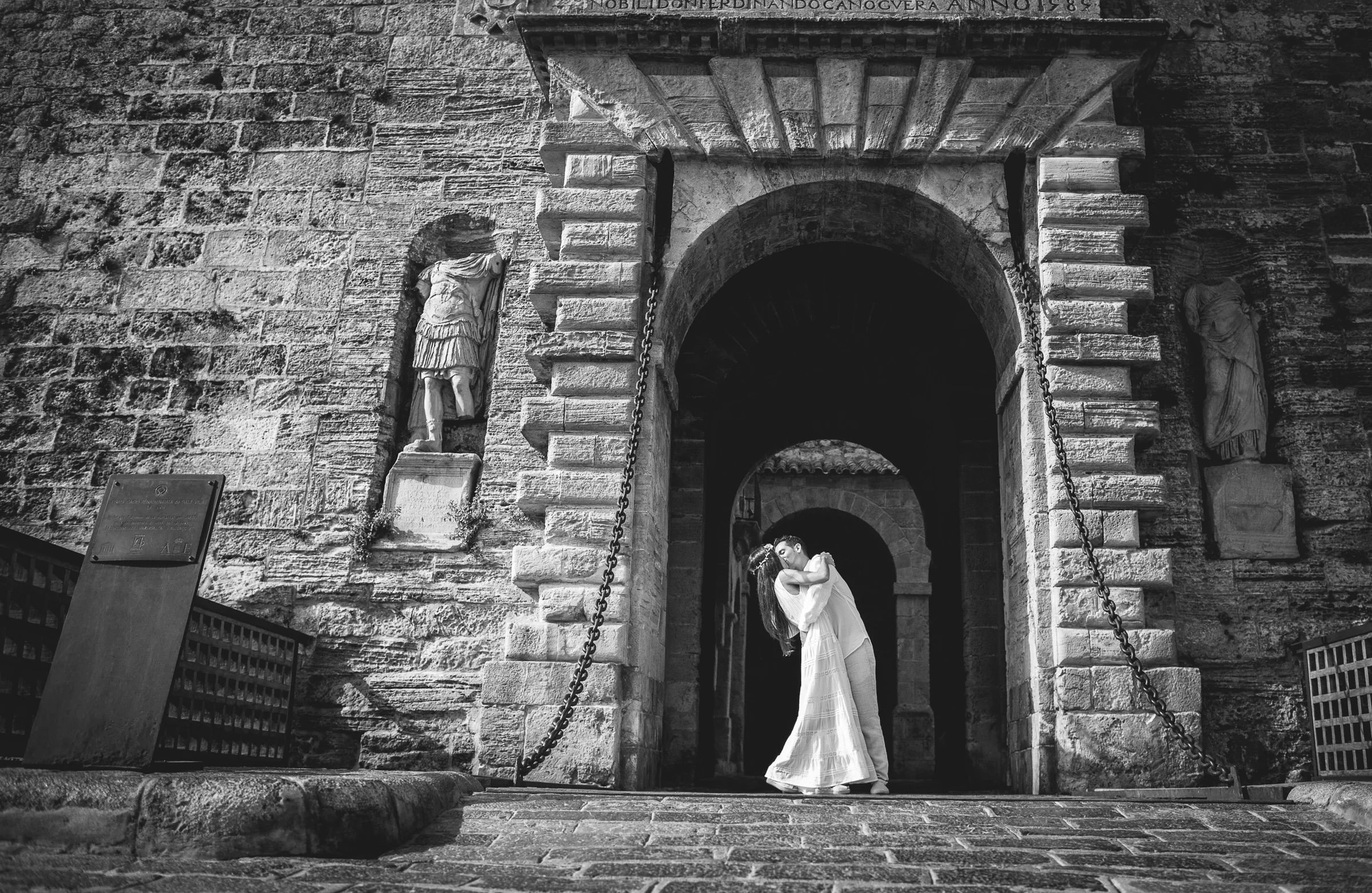 Beso de la pareja bajo la puerta monumental en blanco y negro, postboda de Alba y Jorge en Ibiza fotografiada por Pedro Zamorano.