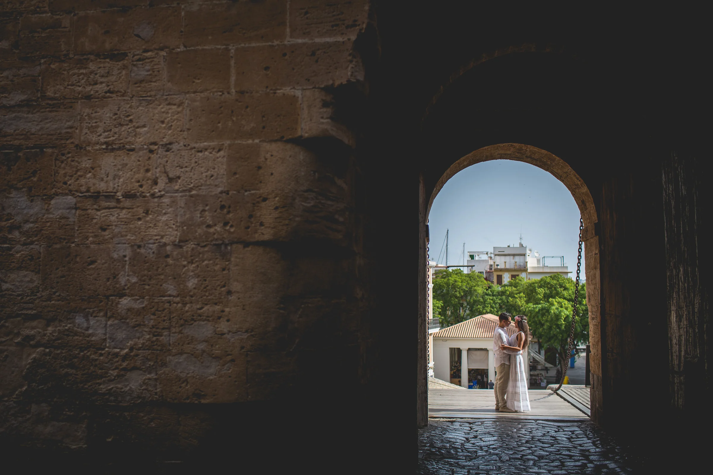 Pareja enmarcada por un arco de piedra con vista a la ciudad, postboda de Alba y Jorge en Ibiza fotografiada por Pedro Zamorano.