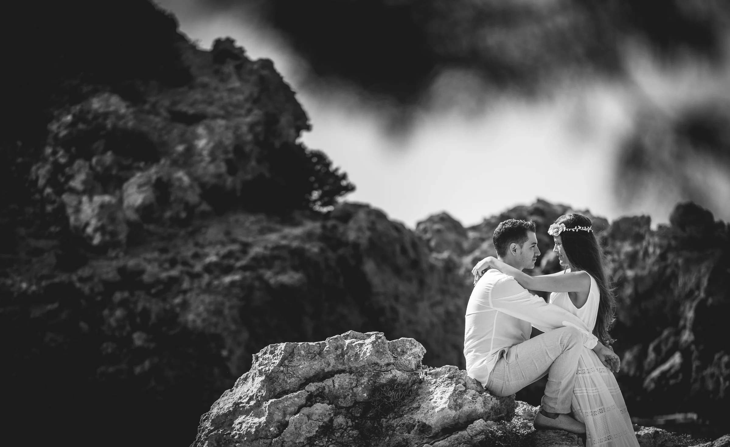 Retrato en blanco y negro de la pareja sentada entre rocas, postboda de Alba y Jorge en Ibiza fotografiada por Pedro Zamorano.