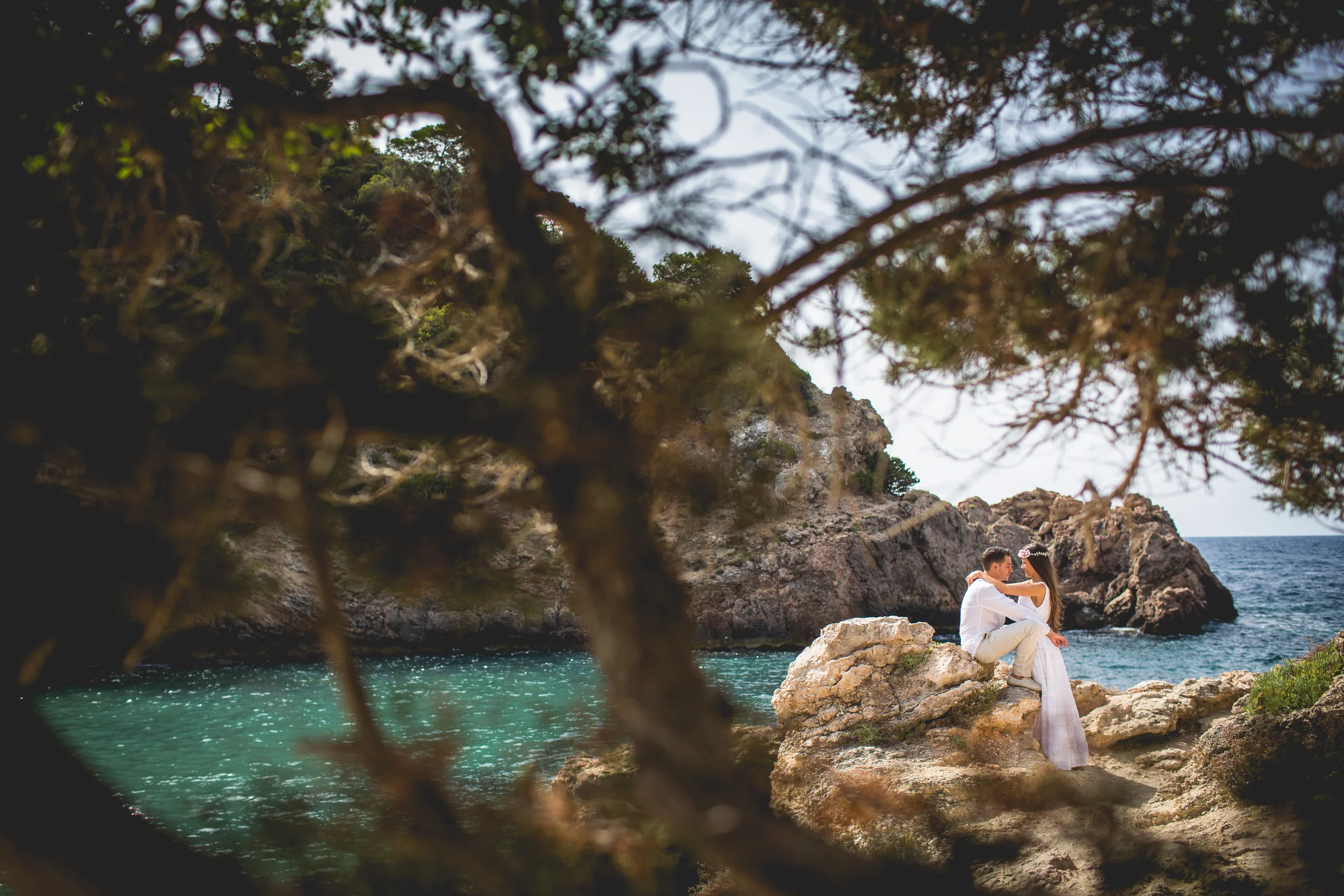 Pareja entre pinos con una cala turquesa al fondo, postboda de Alba y Jorge en Ibiza fotografiada por Pedro Zamorano.
