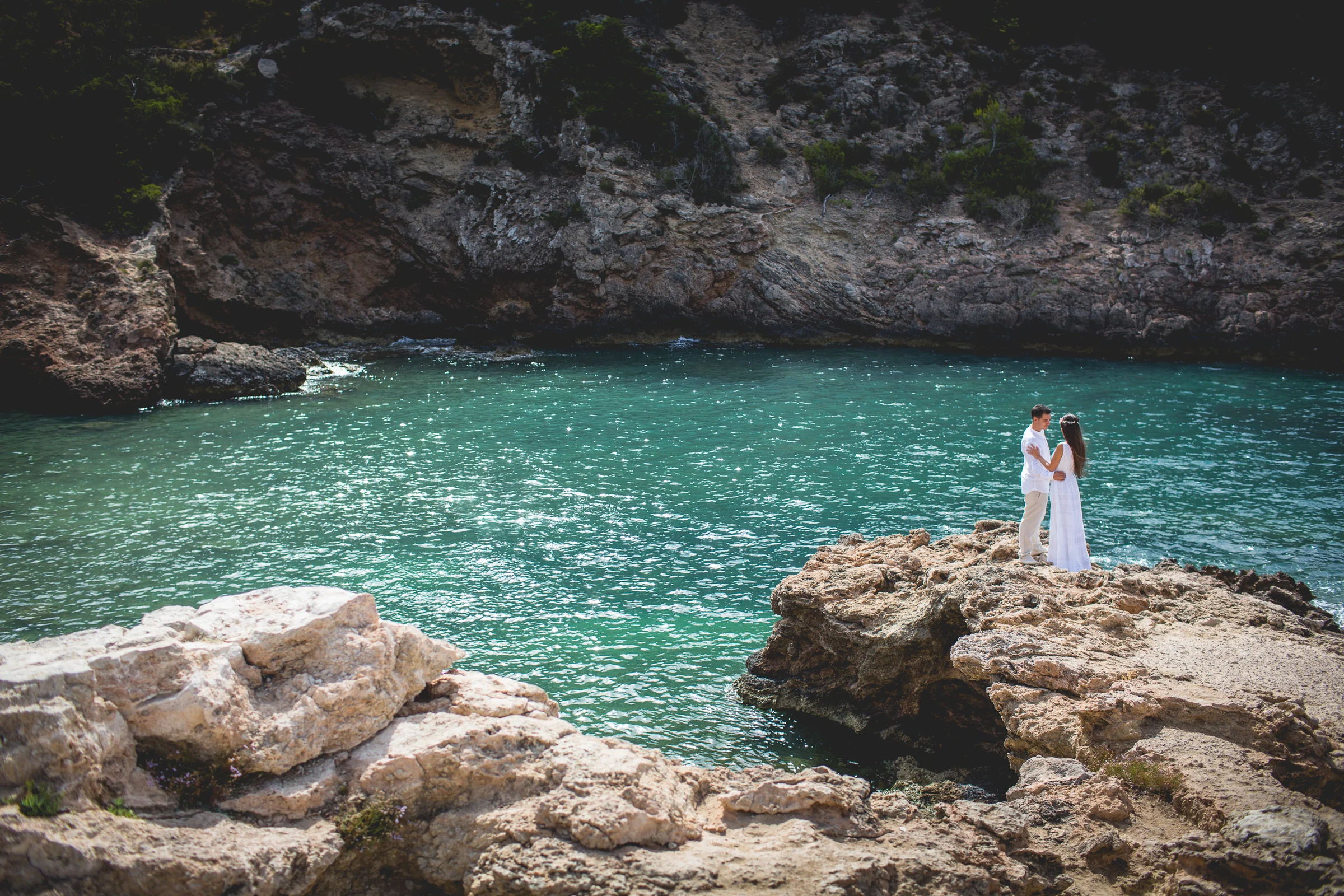 Alba y Jorge sobre un saliente rocoso junto al agua turquesa, postboda de Alba y Jorge en Ibiza fotografiada por Pedro Zamorano.