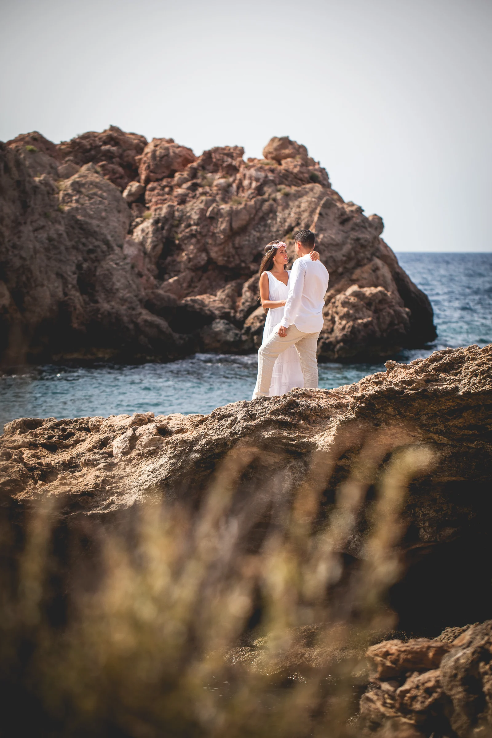 Retrato vertical de Alba y Jorge entre rocas costeras, postboda de Alba y Jorge en Ibiza fotografiada por Pedro Zamorano.