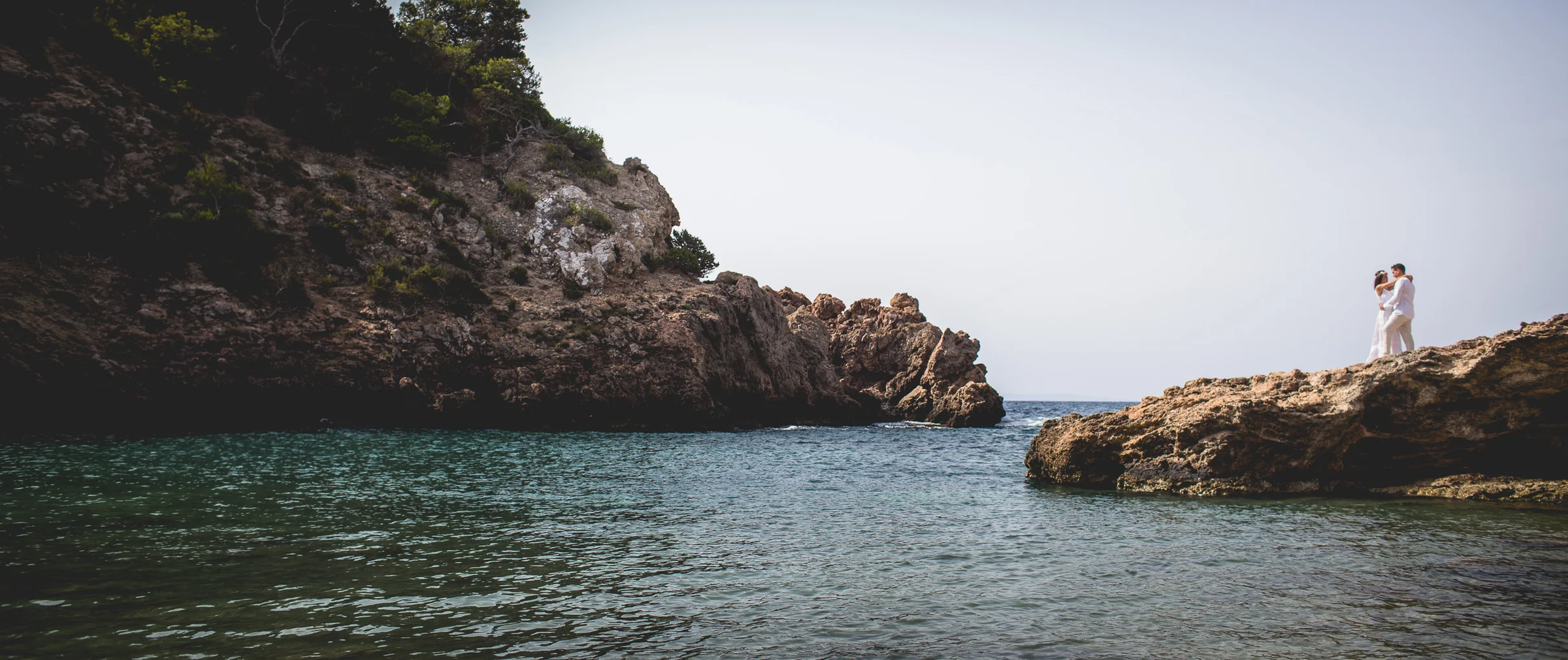 Pareja en una cala de Ibiza vista desde la orilla, postboda de Alba y Jorge en Ibiza fotografiada por Pedro Zamorano.