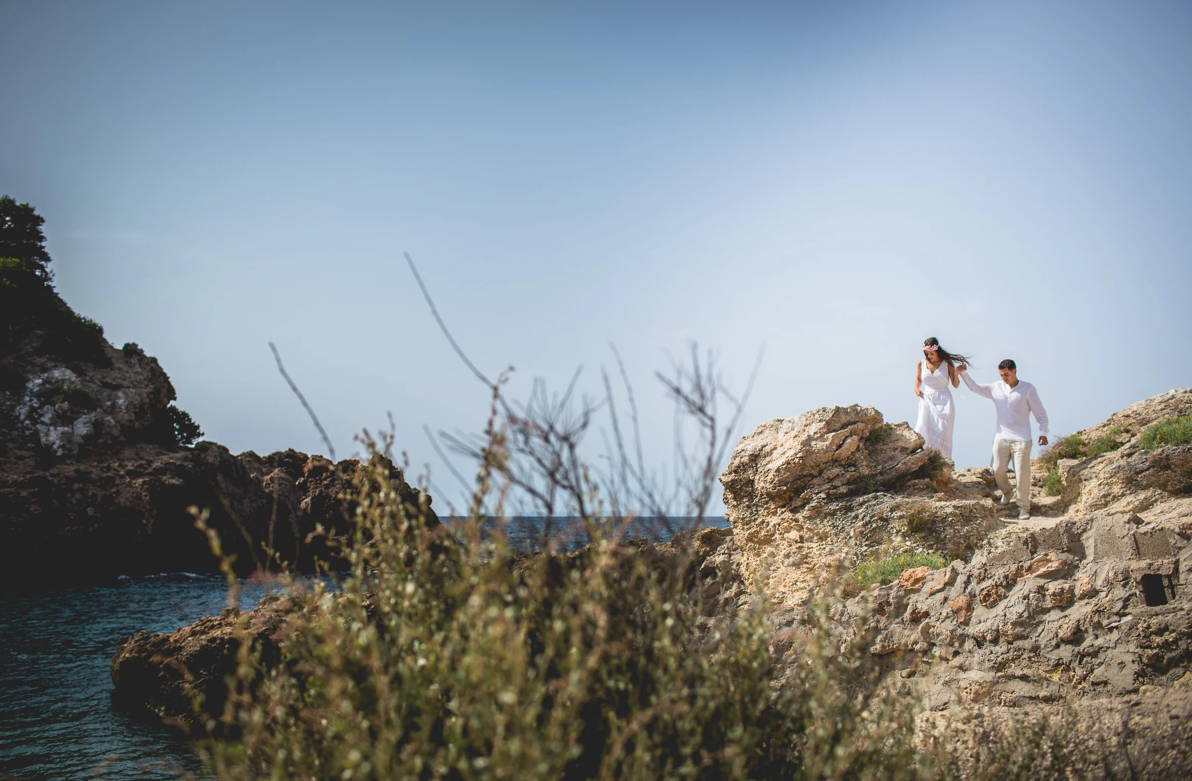 Alba y Jorge caminando por las rocas junto al mar, postboda de Alba y Jorge en Ibiza fotografiada por Pedro Zamorano.