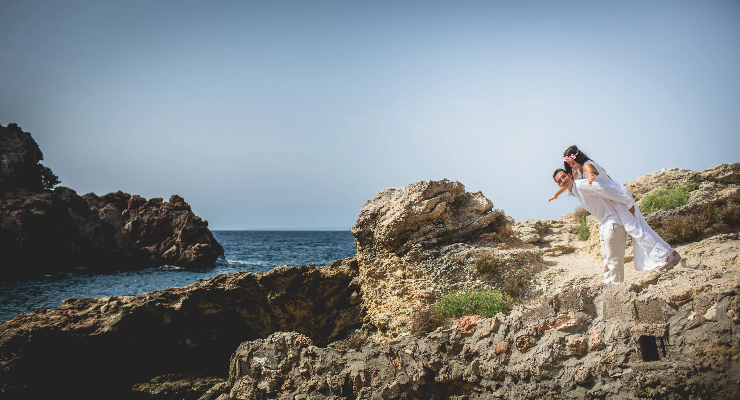 Jorge llevando a Alba a caballito entre rocas, postboda de Alba y Jorge en Ibiza fotografiada por Pedro Zamorano.