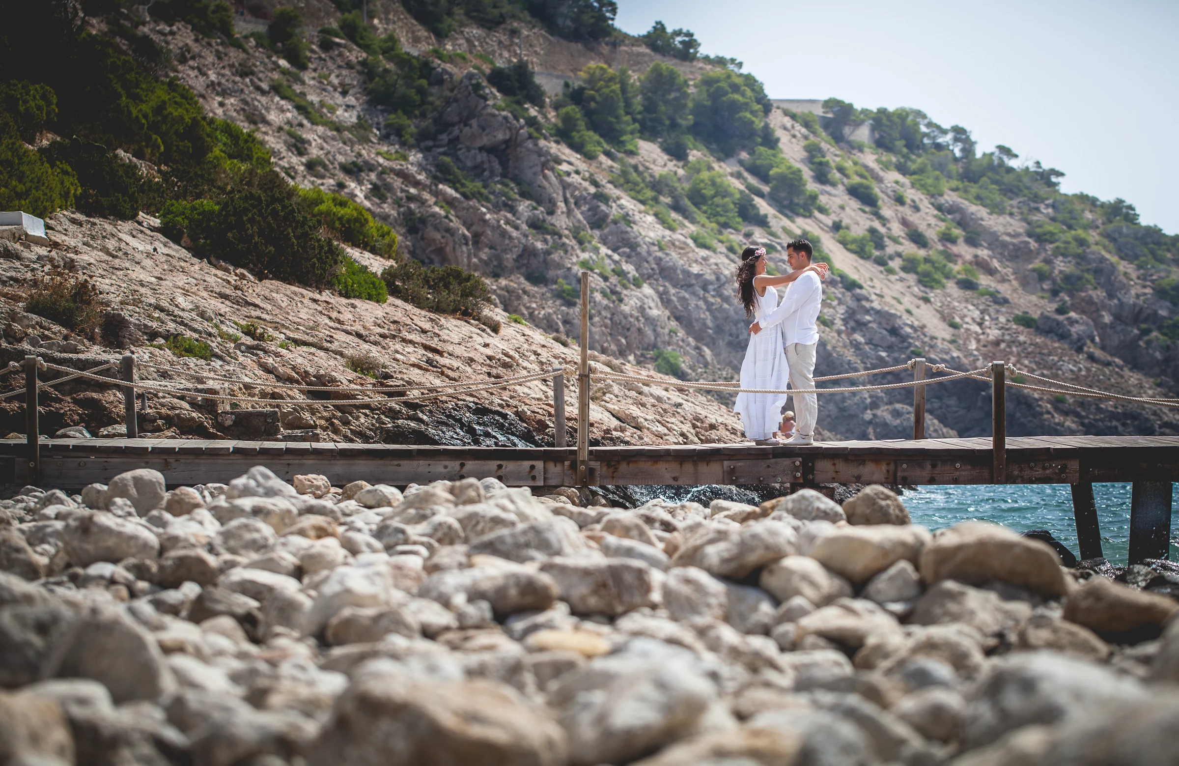 Alba y Jorge sobre una pasarela de madera junto al mar, postboda de Alba y Jorge en Ibiza fotografiada por Pedro Zamorano.