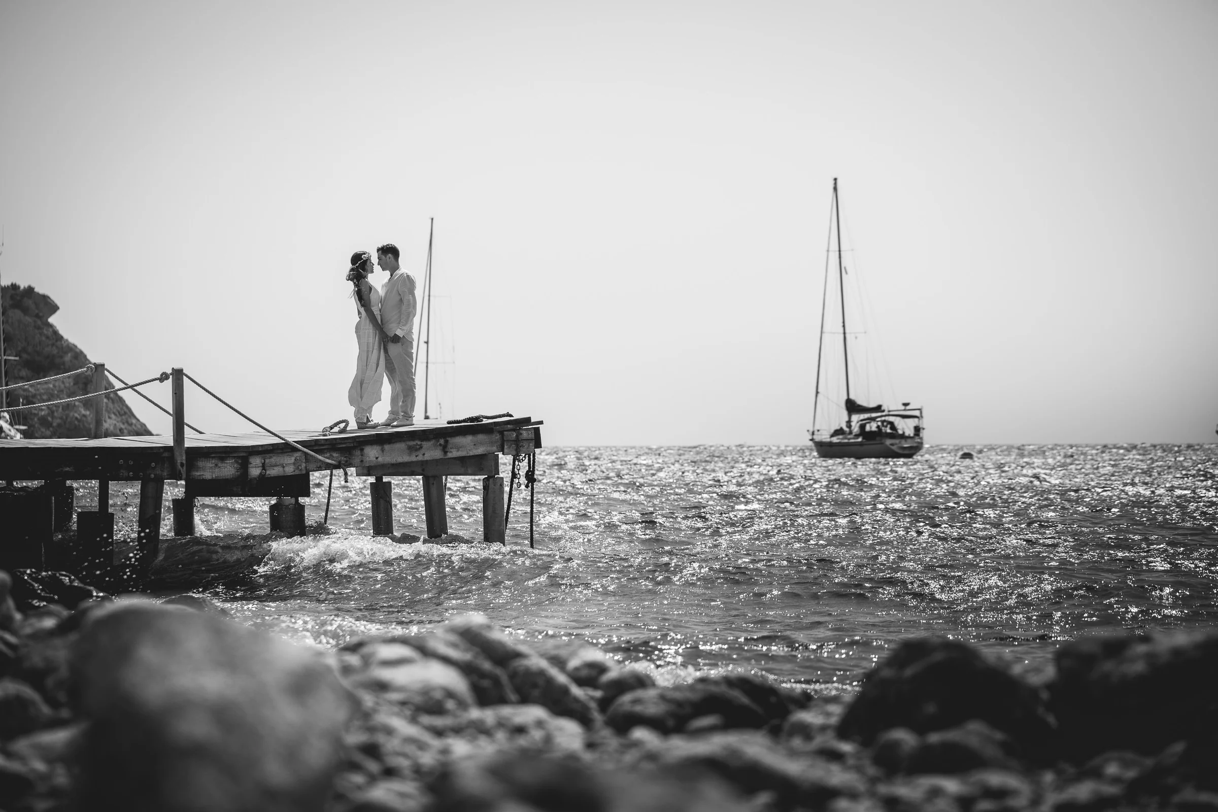 Pareja en un pantalán con velero al fondo en blanco y negro, postboda de Alba y Jorge en Ibiza fotografiada por Pedro Zamorano.