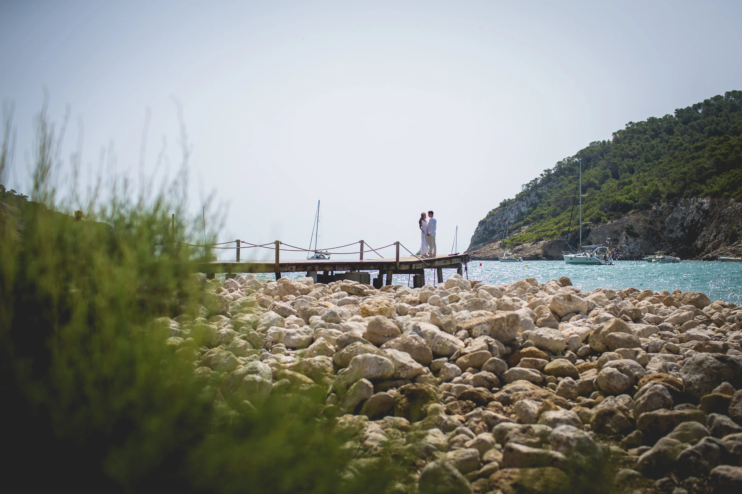 Alba y Jorge en un pantalán vistos entre vegetación, postboda de Alba y Jorge en Ibiza fotografiada por Pedro Zamorano.