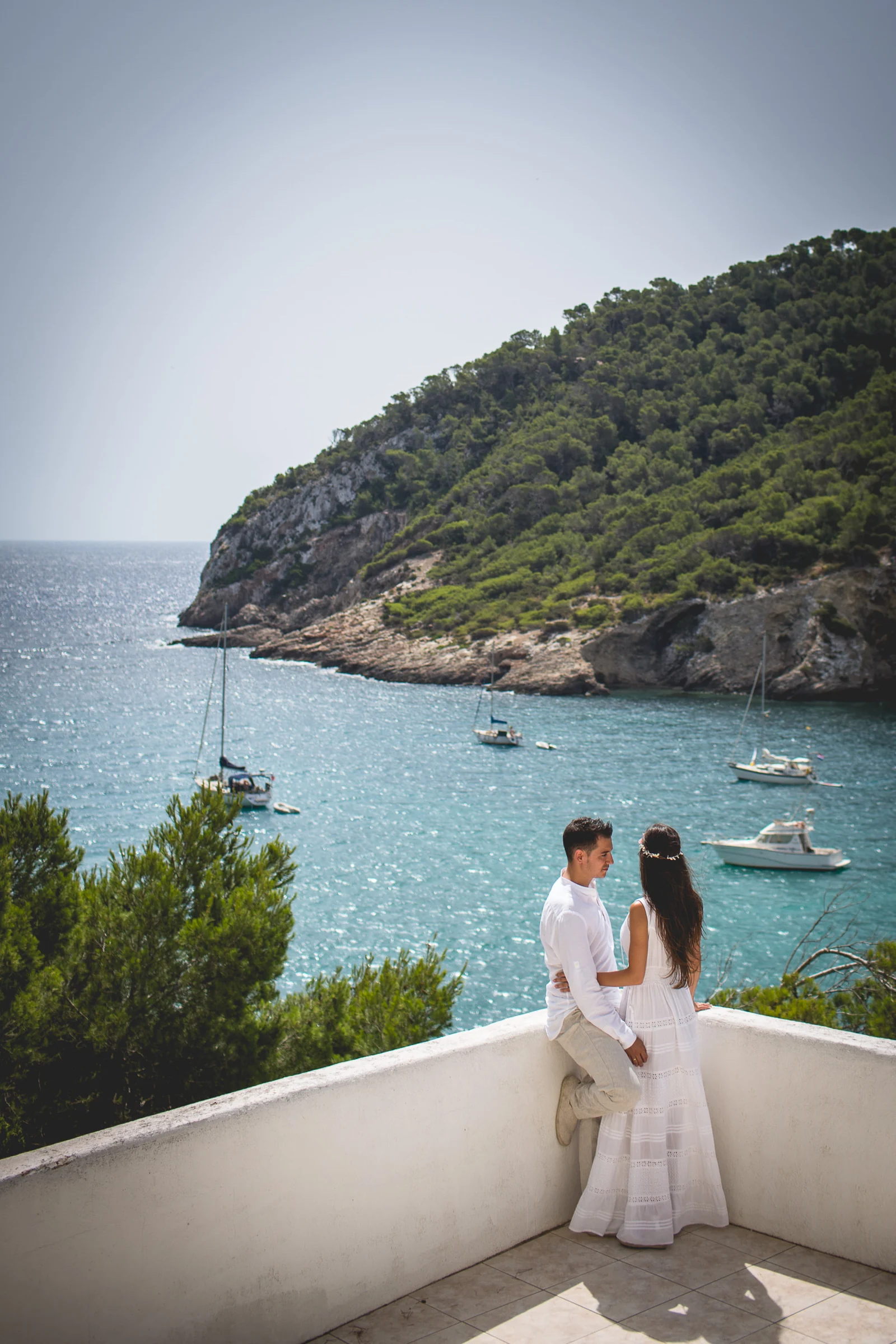 Retrato vertical de la pareja con cala y veleros al fondo, postboda de Alba y Jorge en Ibiza fotografiada por Pedro Zamorano.