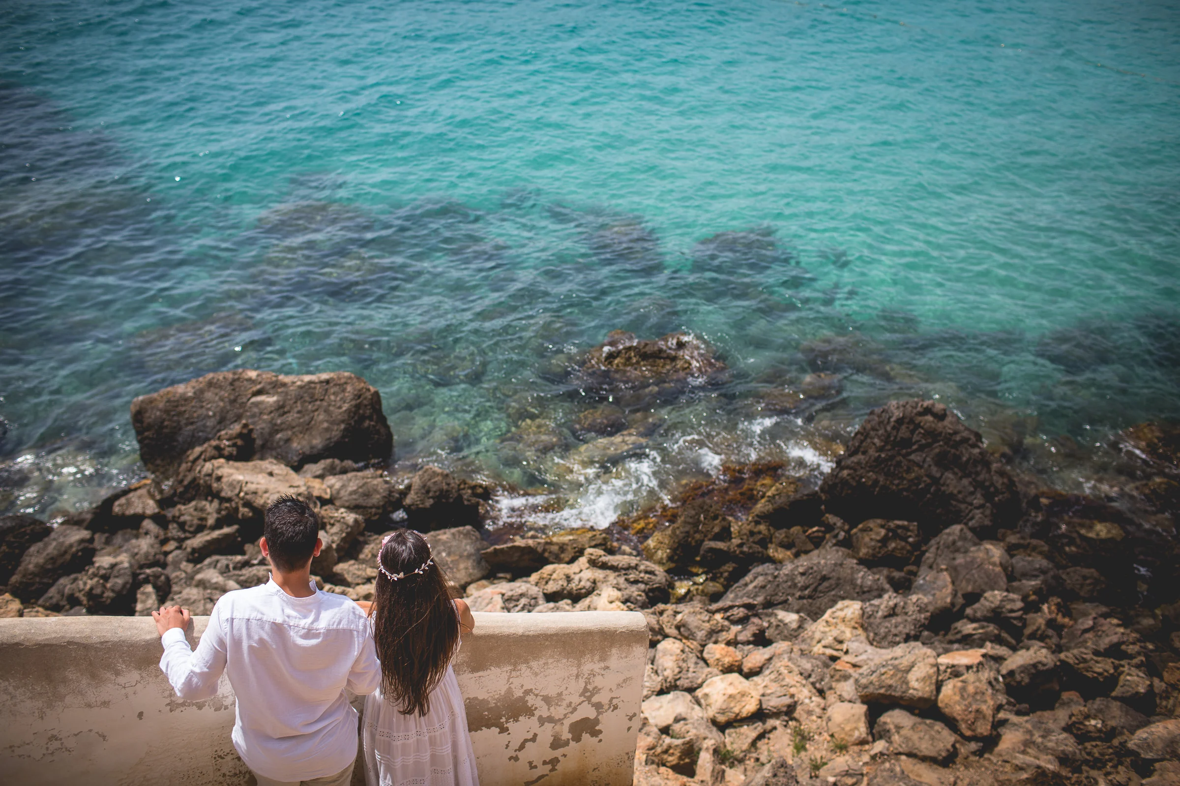Pareja mirando el agua turquesa desde un muro, postboda de Alba y Jorge en Ibiza fotografiada por Pedro Zamorano.