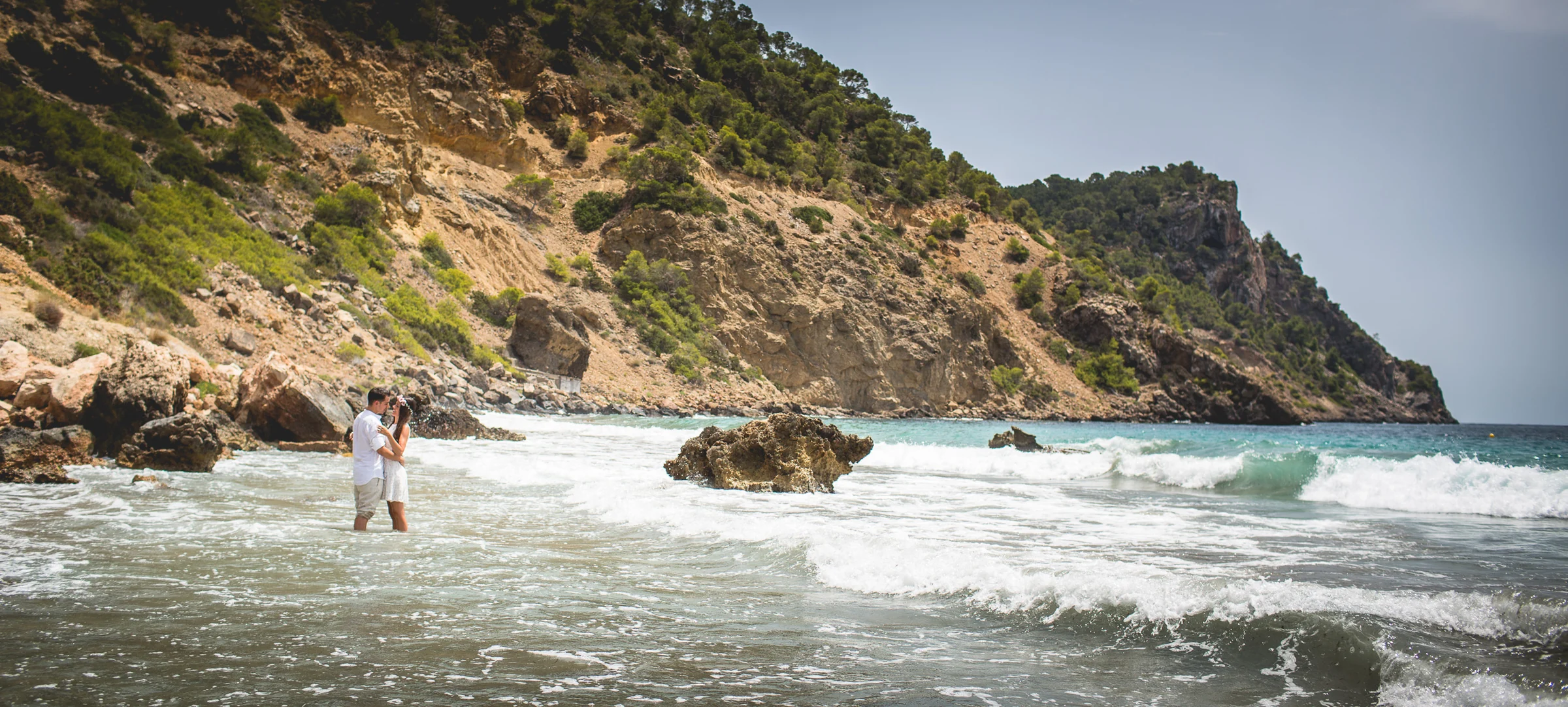 Alba y Jorge dentro del agua con acantilados al fondo, postboda de Alba y Jorge en Ibiza fotografiada por Pedro Zamorano.