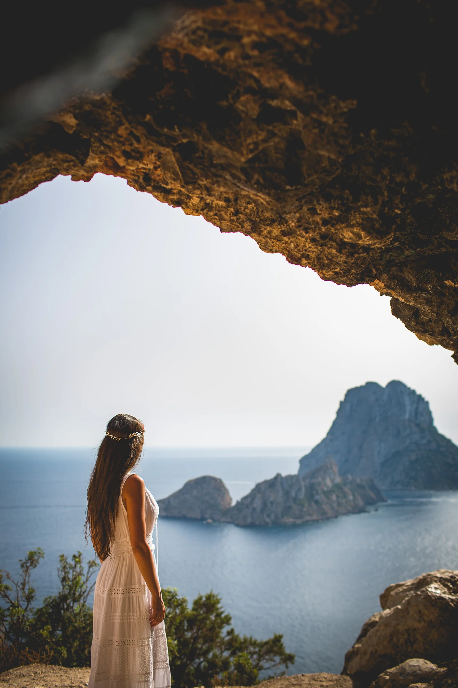 Retrato vertical de Alba contemplando Es Vedrà bajo una roca, postboda de Alba y Jorge en Ibiza fotografiada por Pedro Zamorano.