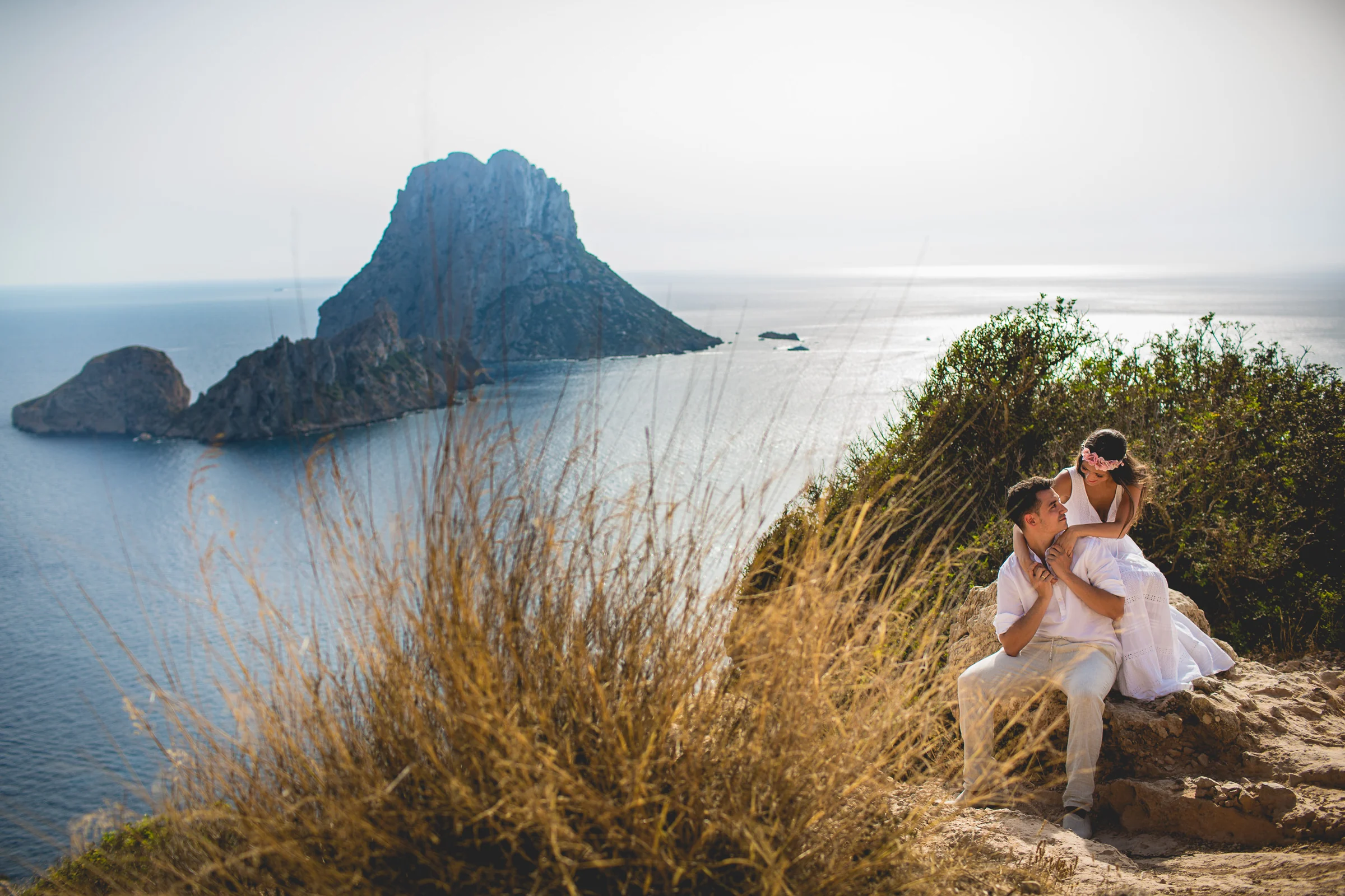 Pareja sentada entre vegetación con Es Vedrà al fondo, postboda de Alba y Jorge en Ibiza fotografiada por Pedro Zamorano.