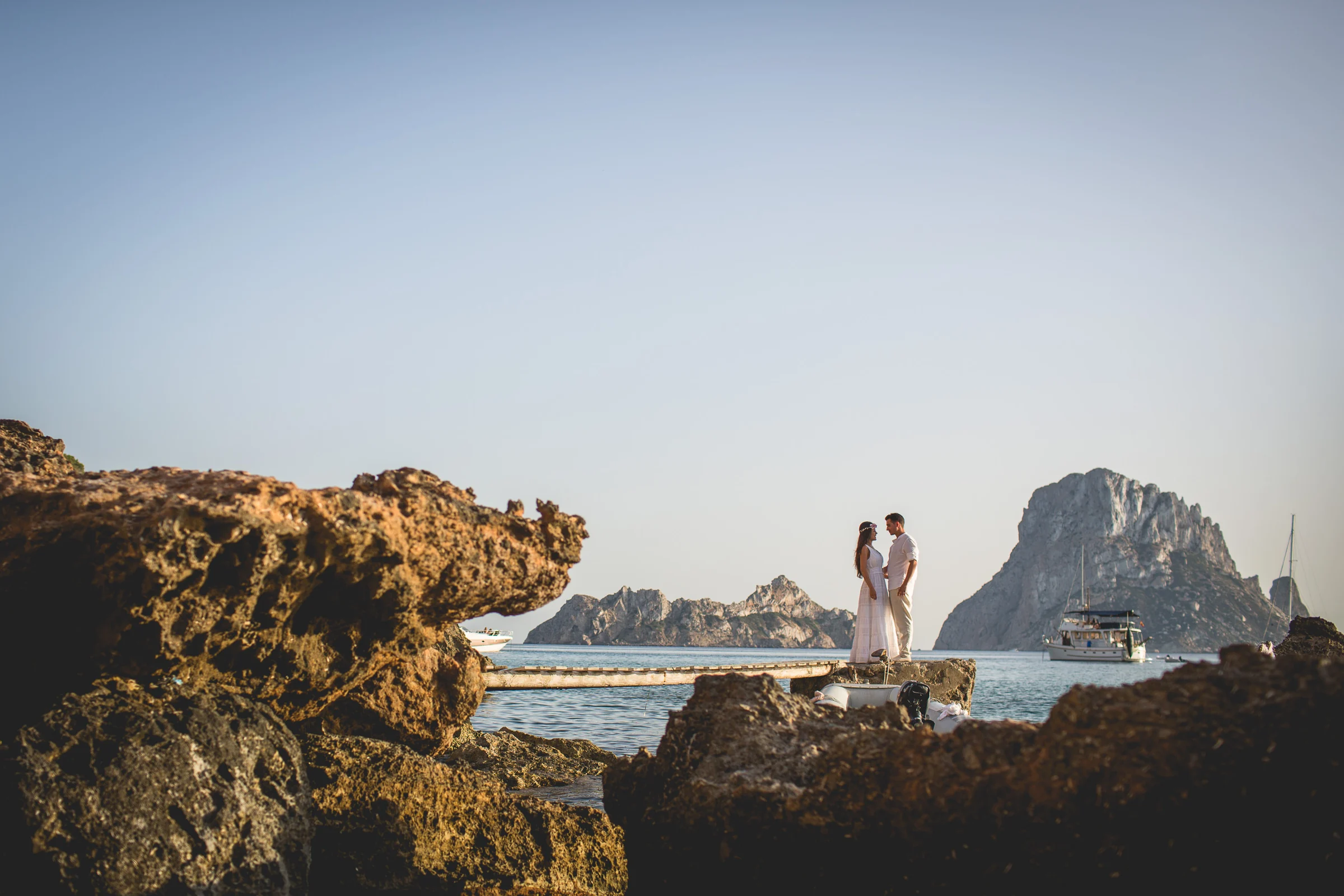 Alba y Jorge enmarcados entre rocas con Es Vedrà al fondo, postboda de Alba y Jorge en Ibiza fotografiada por Pedro Zamorano.