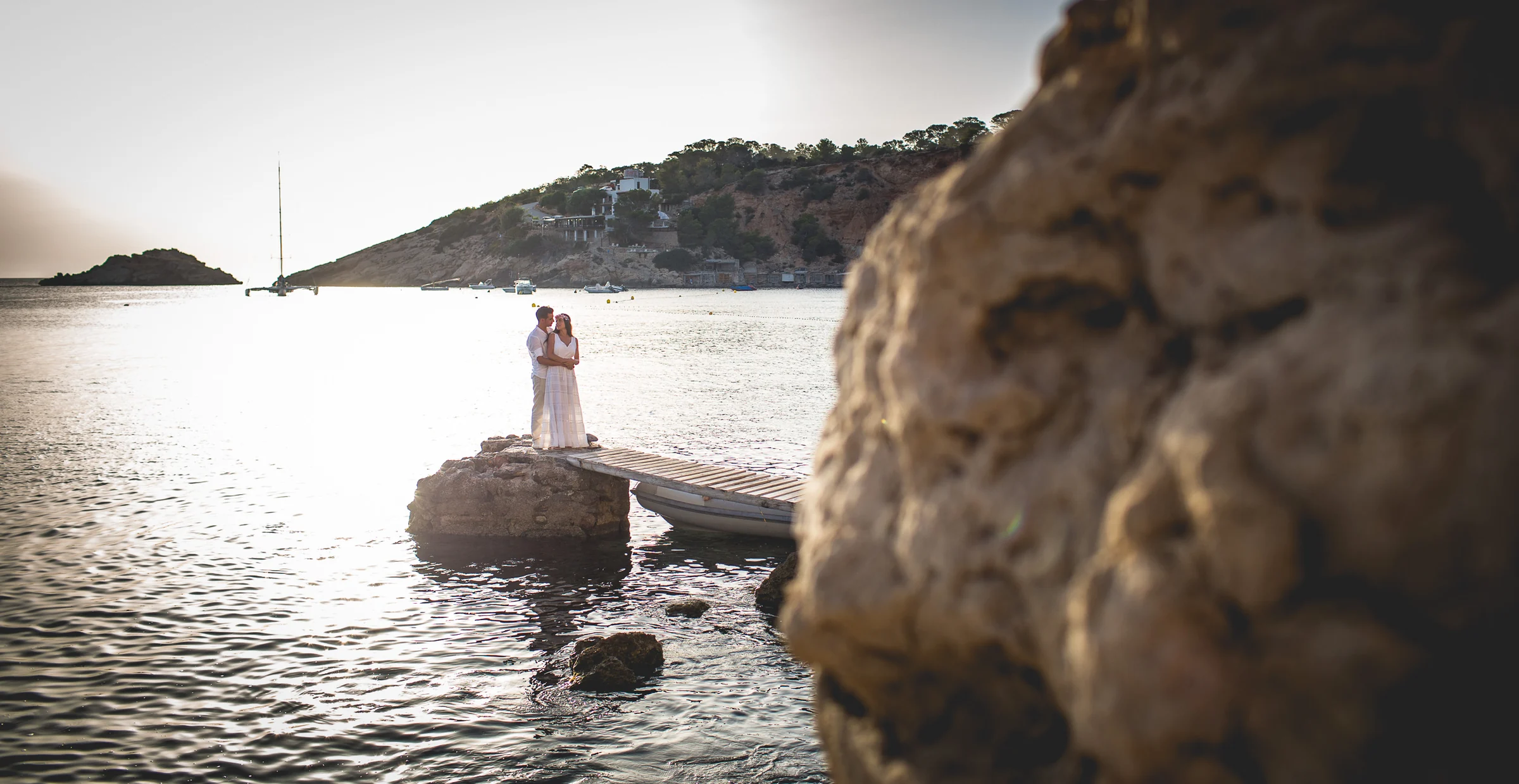 Pareja pequeña junto al mar con roca en primer plano, postboda de Alba y Jorge en Ibiza fotografiada por Pedro Zamorano.