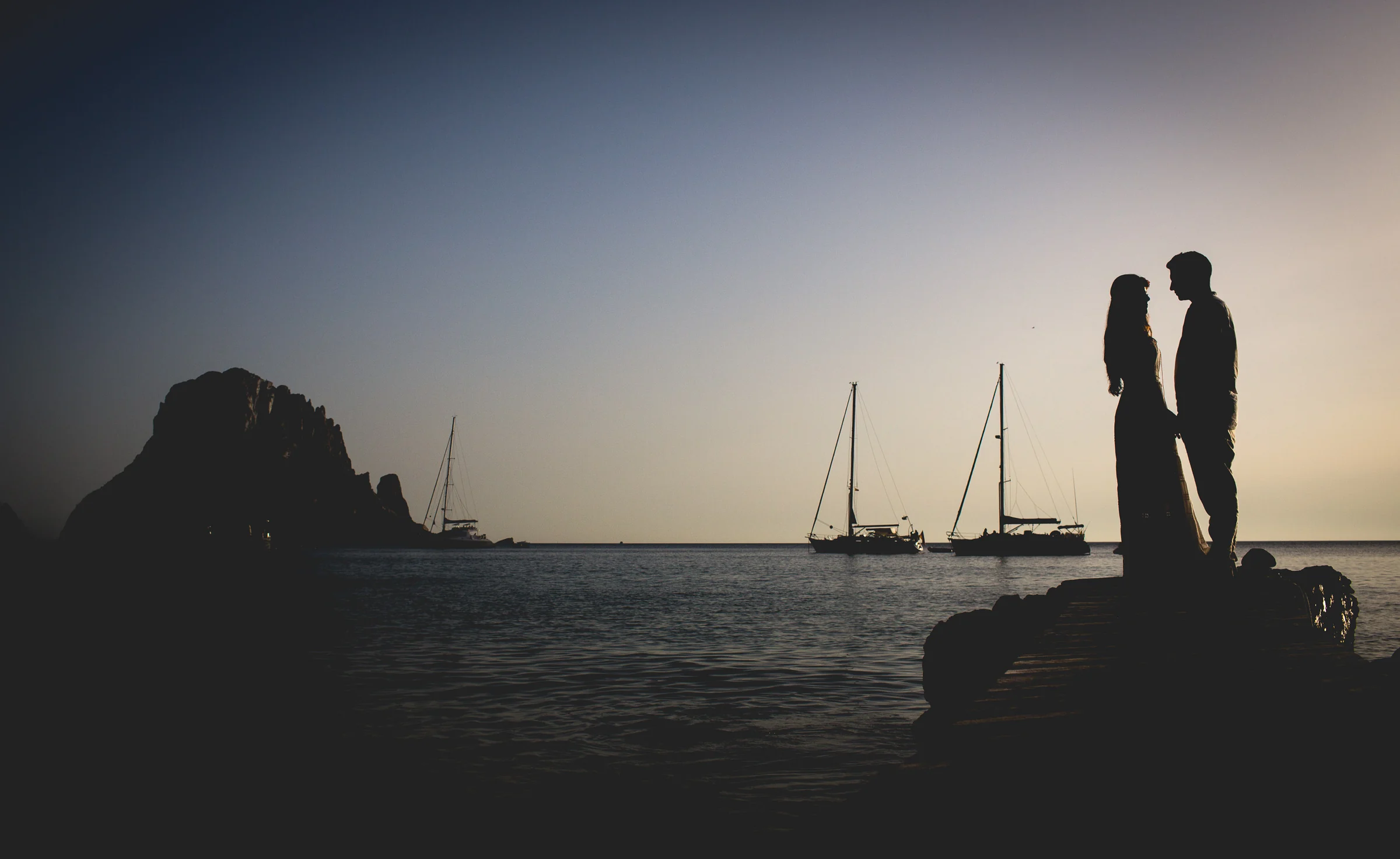 Silueta de Alba y Jorge con veleros al atardecer, postboda de Alba y Jorge en Ibiza fotografiada por Pedro Zamorano.