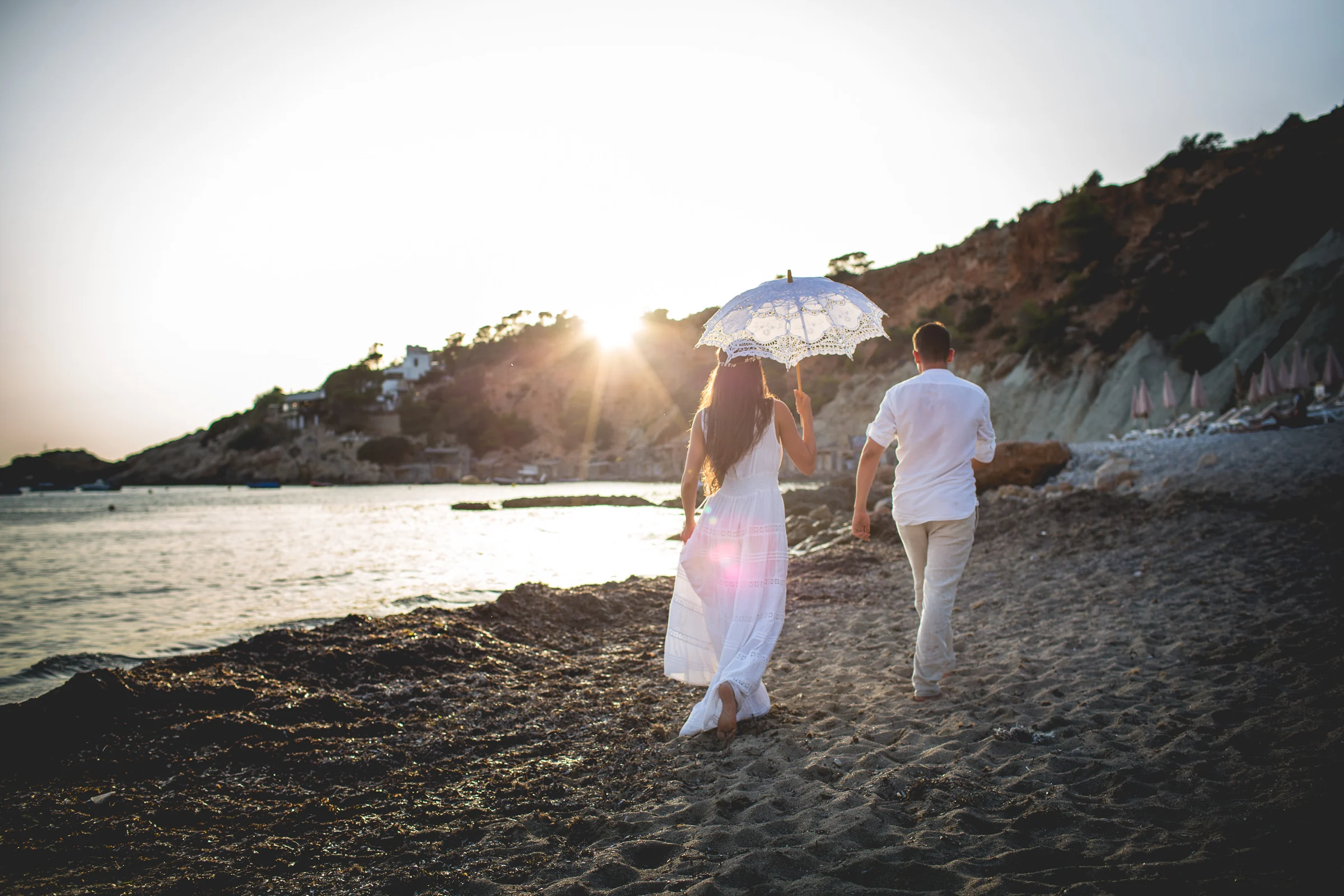 Alba caminando con sombrilla de encaje junto a Jorge, postboda de Alba y Jorge en Ibiza fotografiada por Pedro Zamorano.