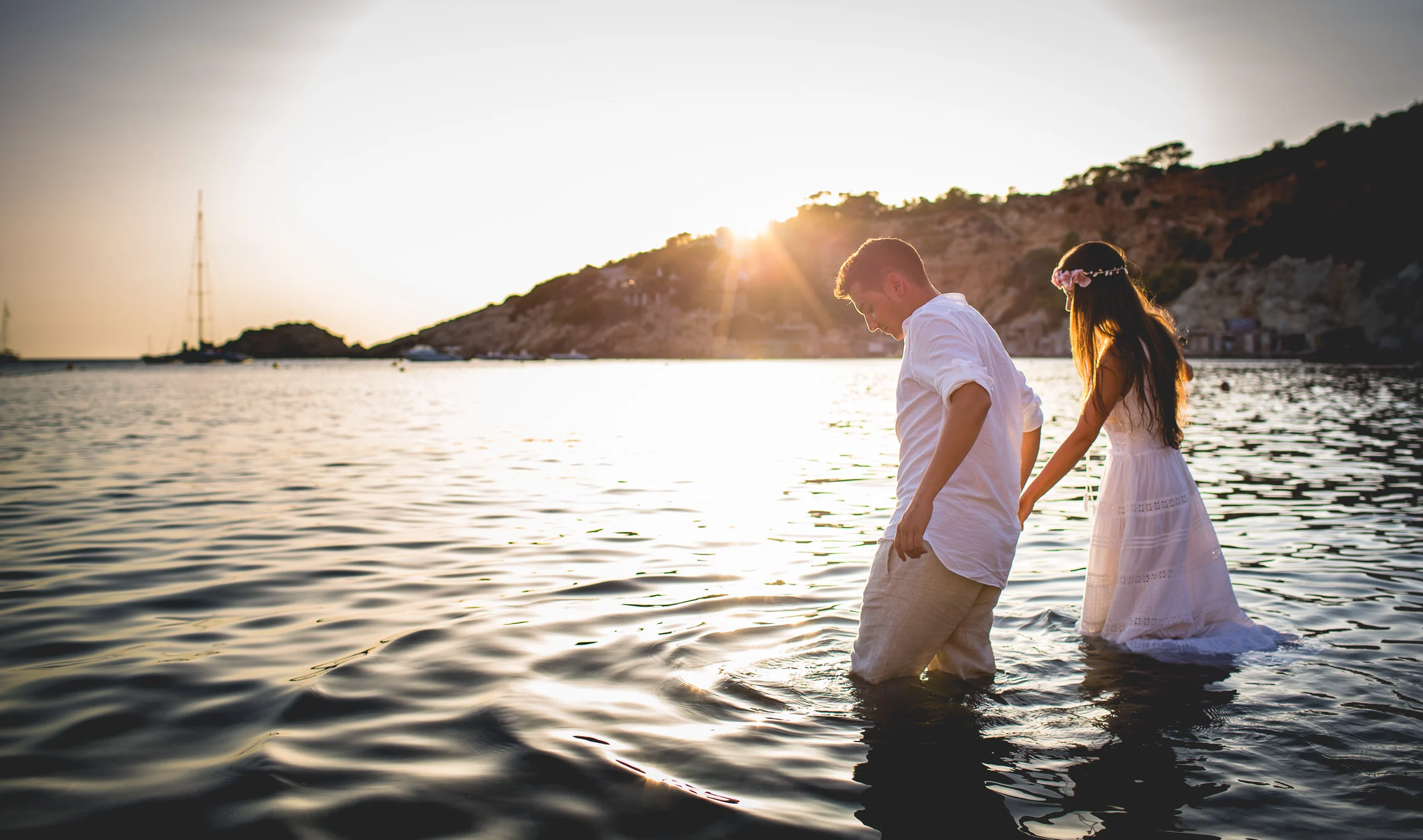 Alba y Jorge caminando dentro del agua al ponerse el sol, postboda de Alba y Jorge en Ibiza fotografiada por Pedro Zamorano.