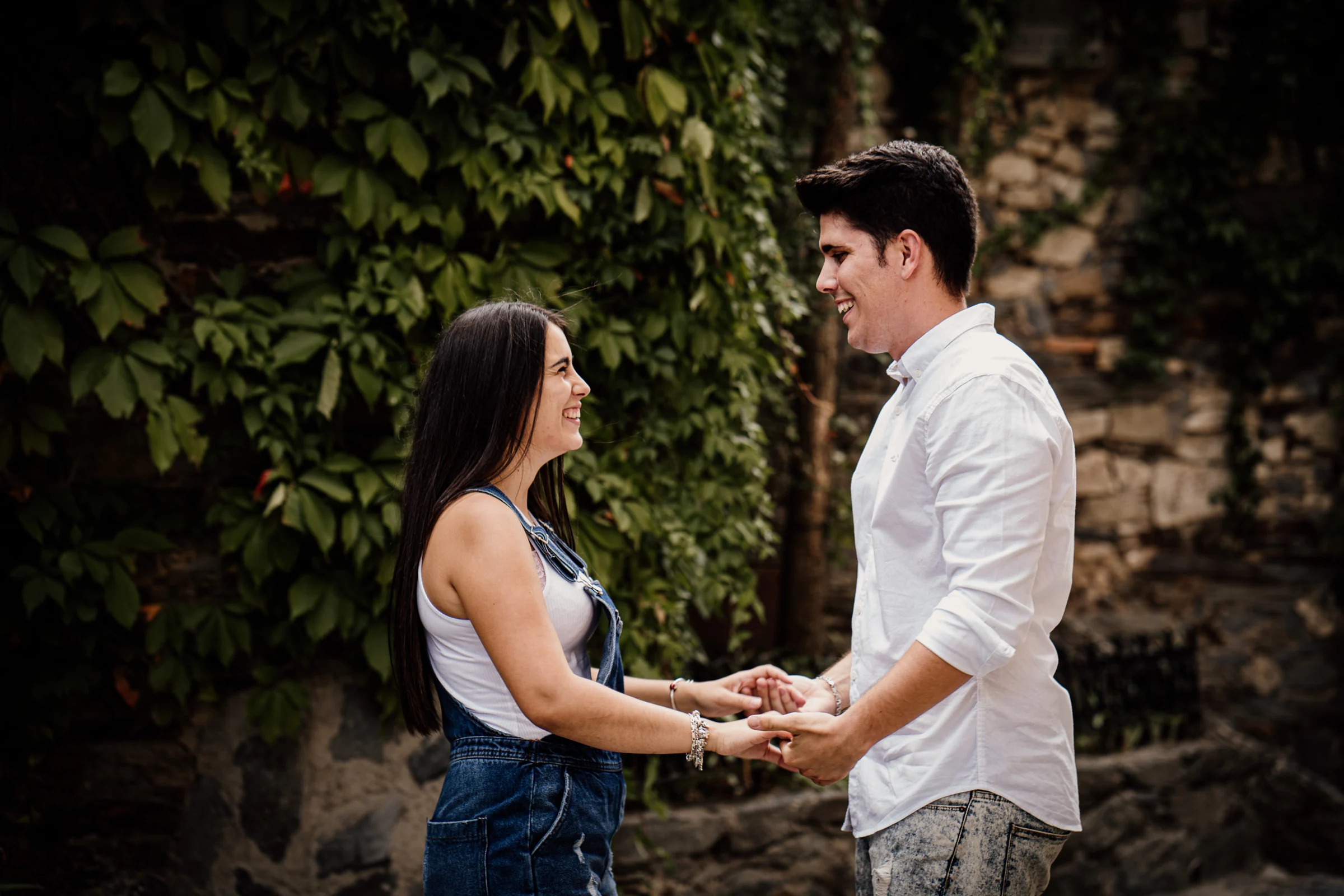 Aritz y Laura se miran sonrientes entre muros de piedra y hiedra durante su preboda en Patones.