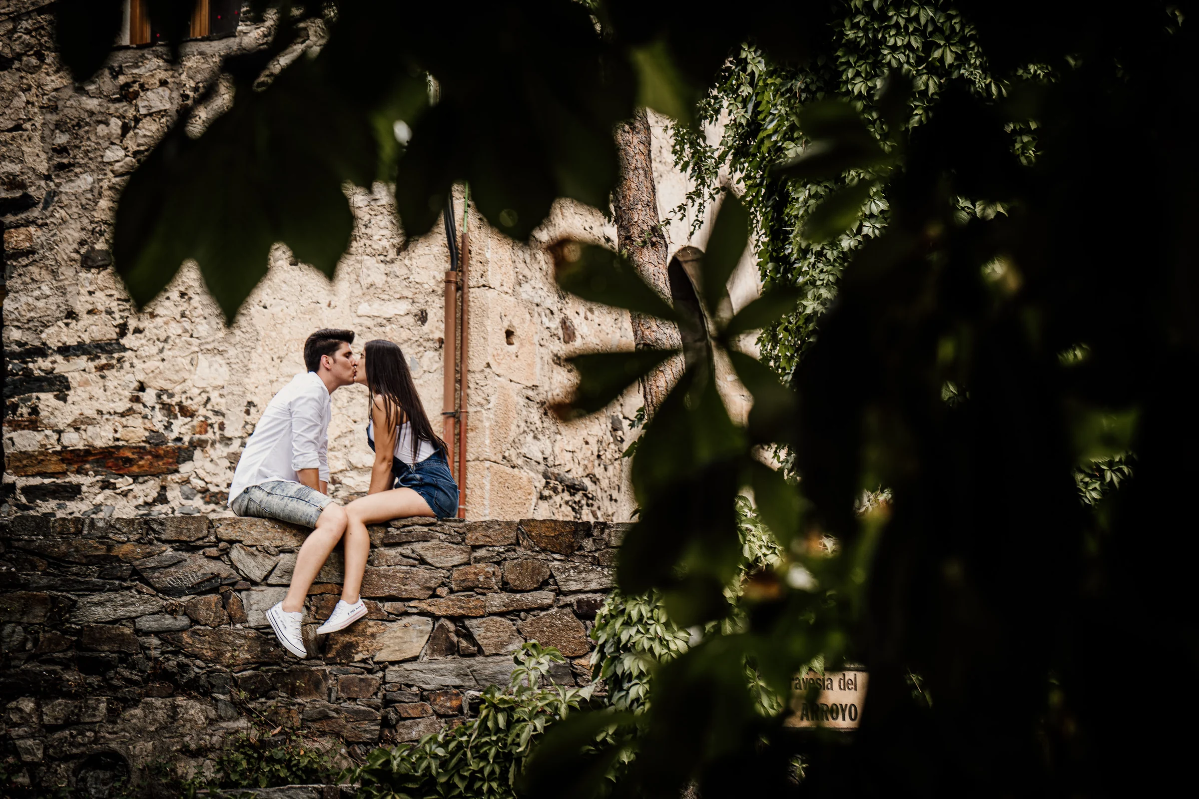 Aritz y Laura se besan sentados sobre un muro de piedra y rodeados de vegetación durante su preboda en Patones.