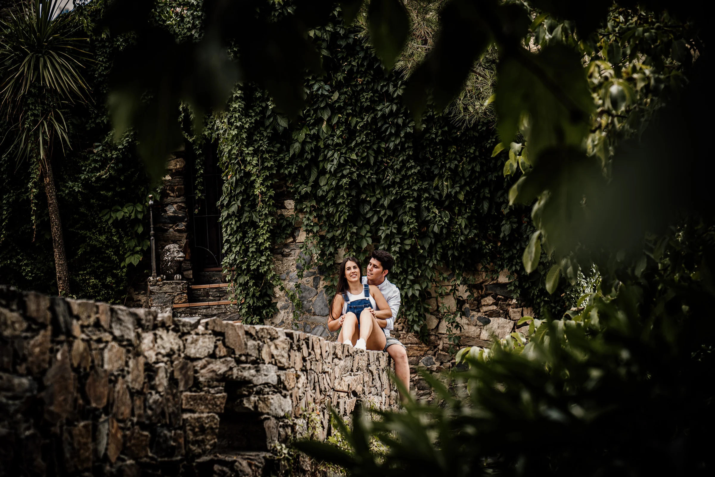 Aritz y Laura aparecen sentados entre la vegetación y la arquitectura de piedra durante su preboda en Patones.
