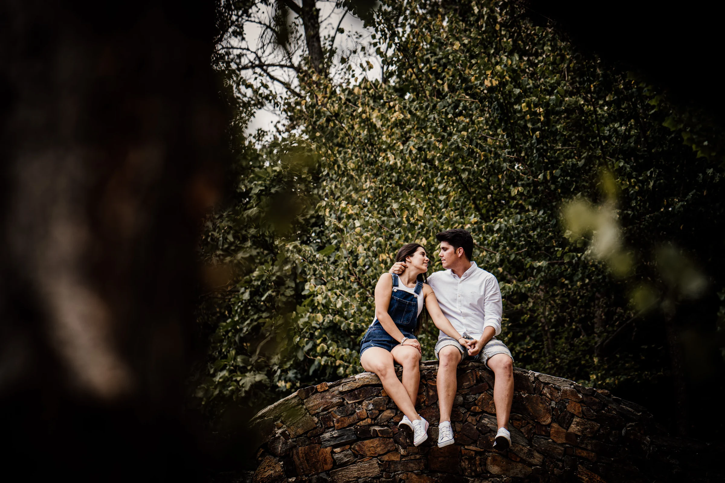 Aritz y Laura conversan sentados sobre un pequeño puente de piedra durante su preboda en Patones.