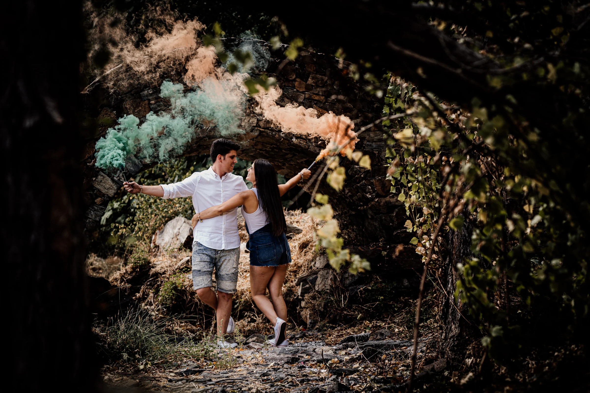 Aritz y Laura sostienen bengalas de humo de colores bajo un arco de piedra durante su preboda en Patones.