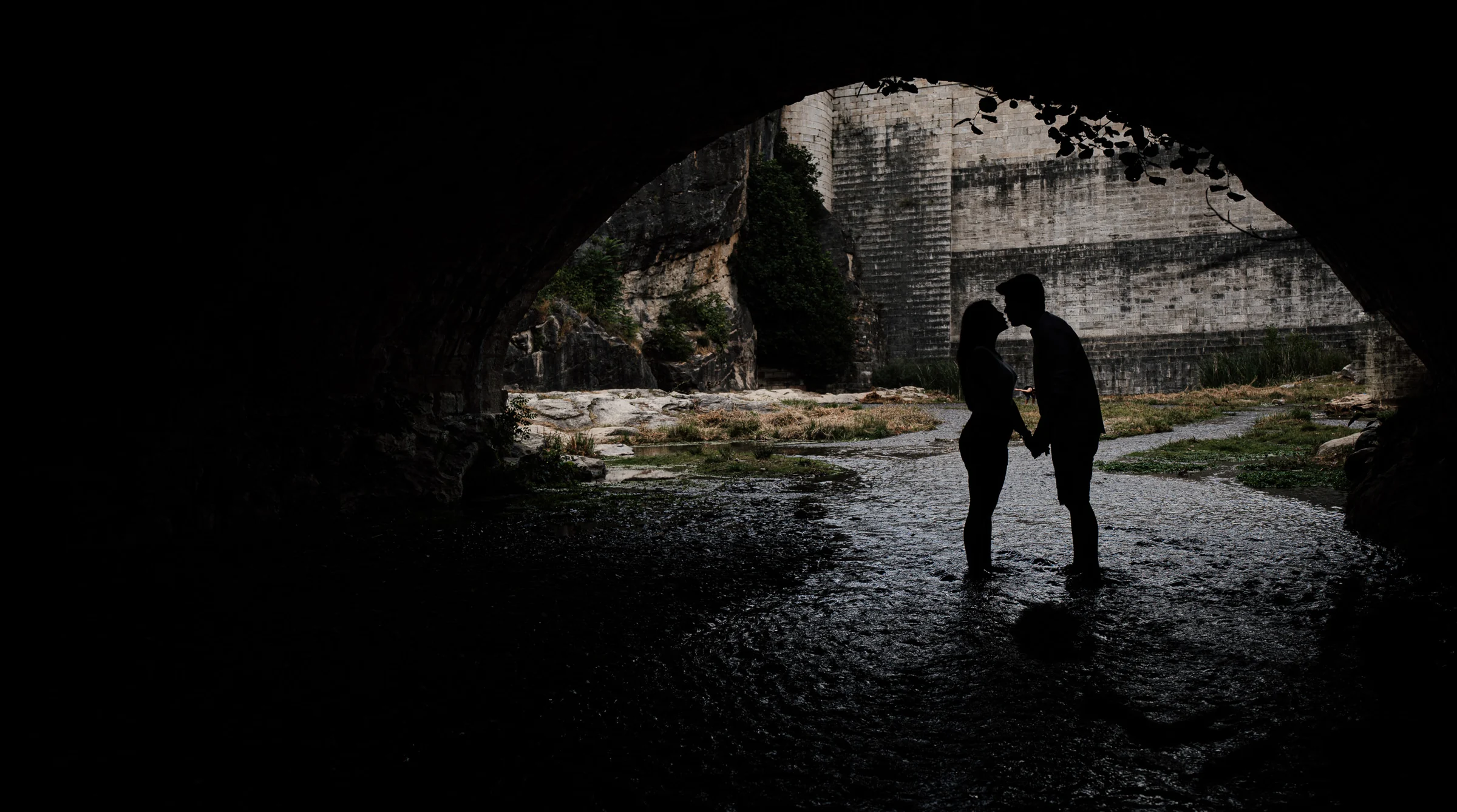 Silueta de Aritz y Laura cogidos de la mano bajo un túnel o arco oscuro durante su preboda en Patones.