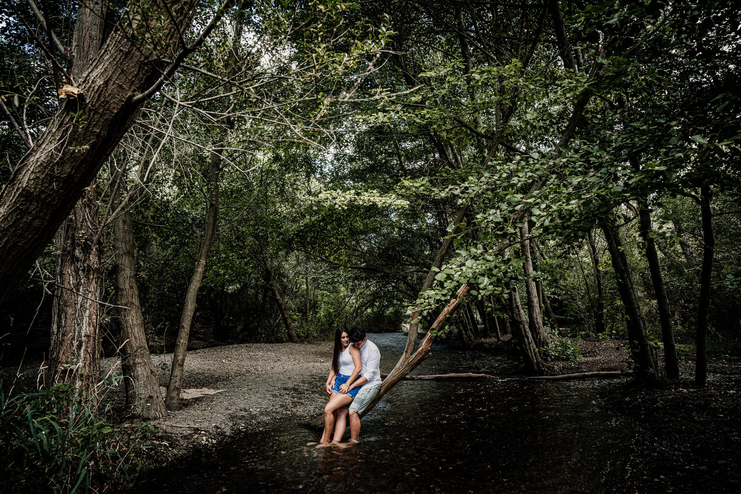 Aritz y Laura se sientan juntos dentro de un pequeño arroyo rodeado de árboles durante su preboda en Patones.