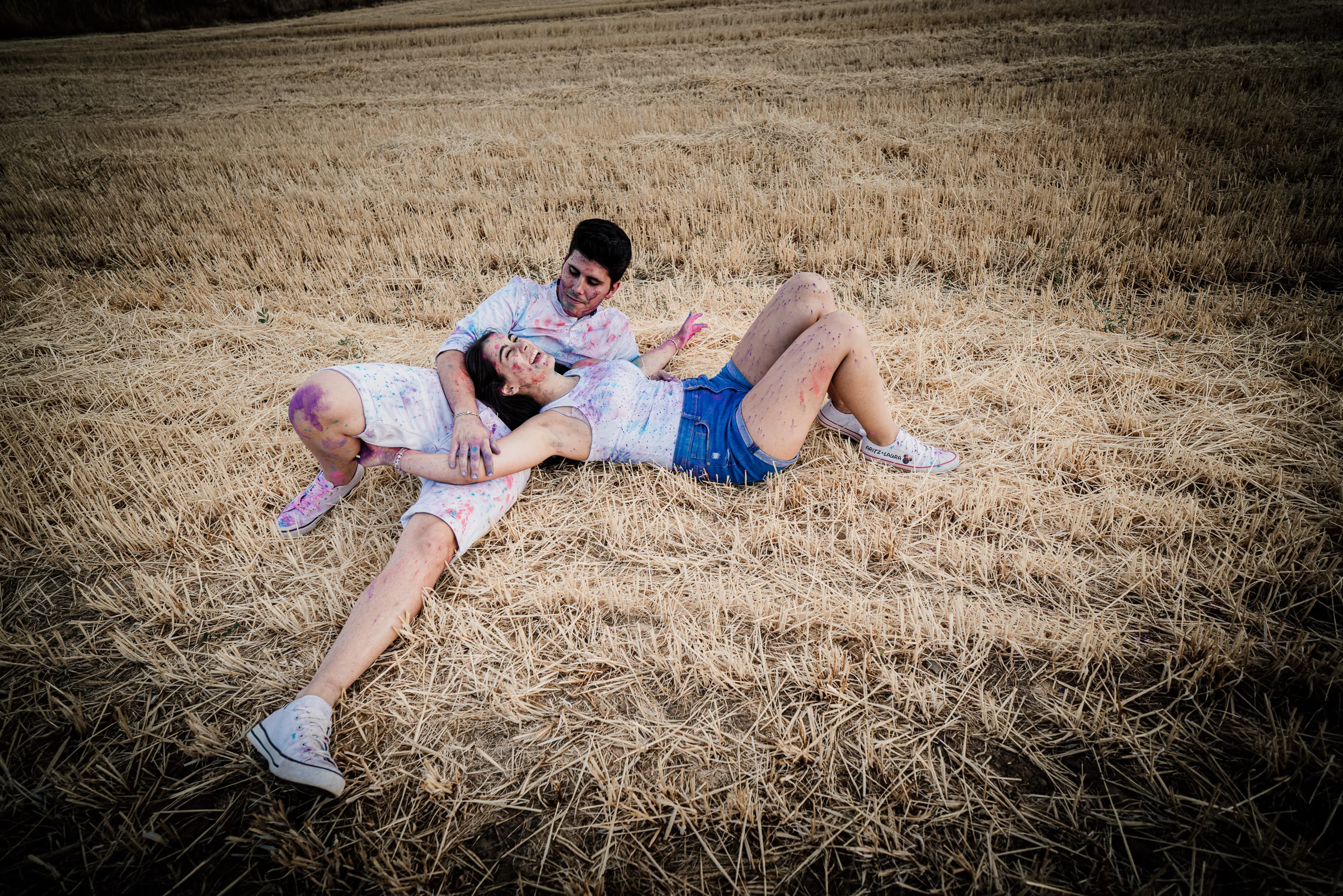Aritz y Laura descansan tumbados sobre la paja y cubiertos de pintura tras su preboda en los campos de Patones.
