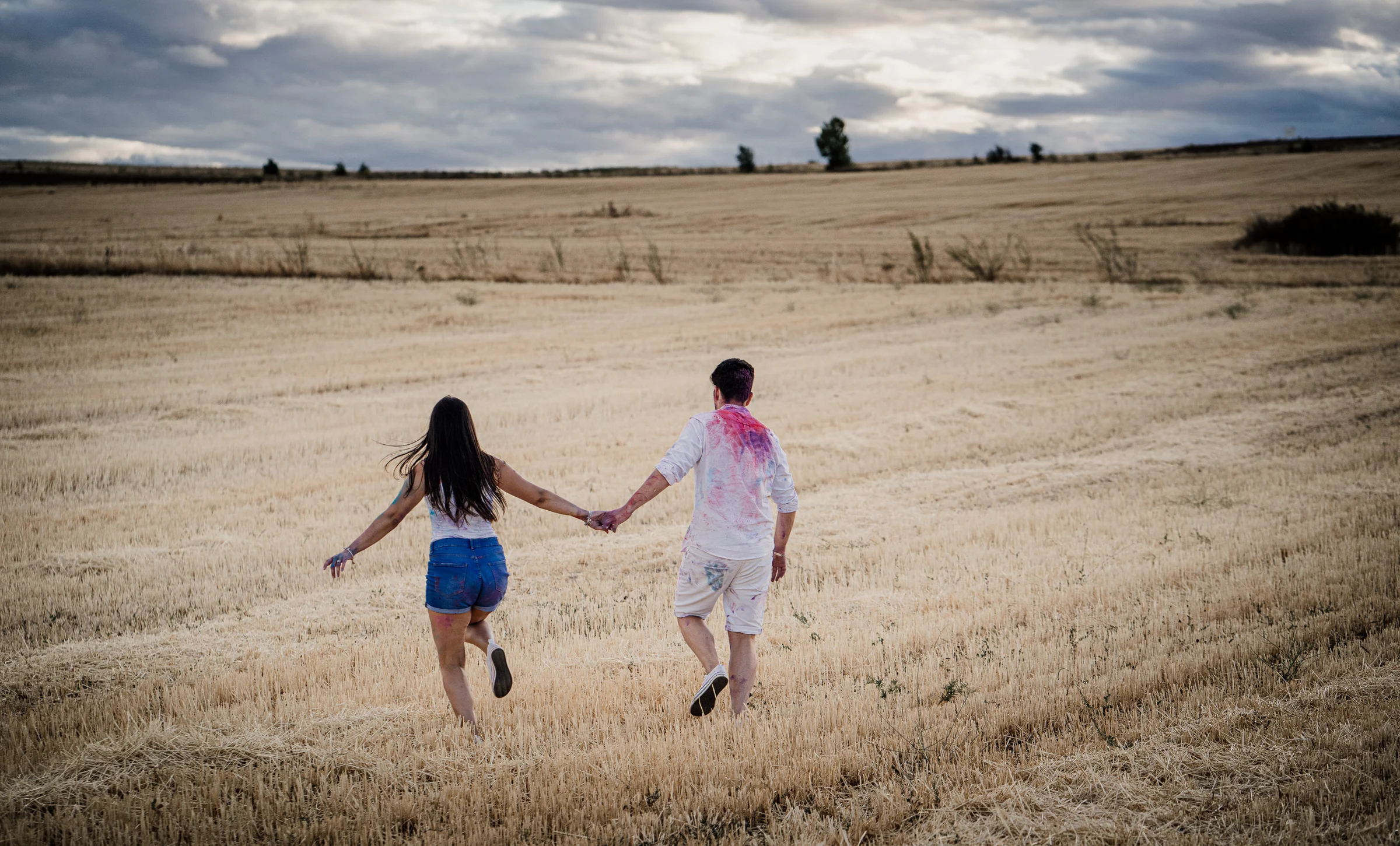 Aritz y Laura corren de la mano hacia el campo después de jugar con pintura durante su preboda en Patones.