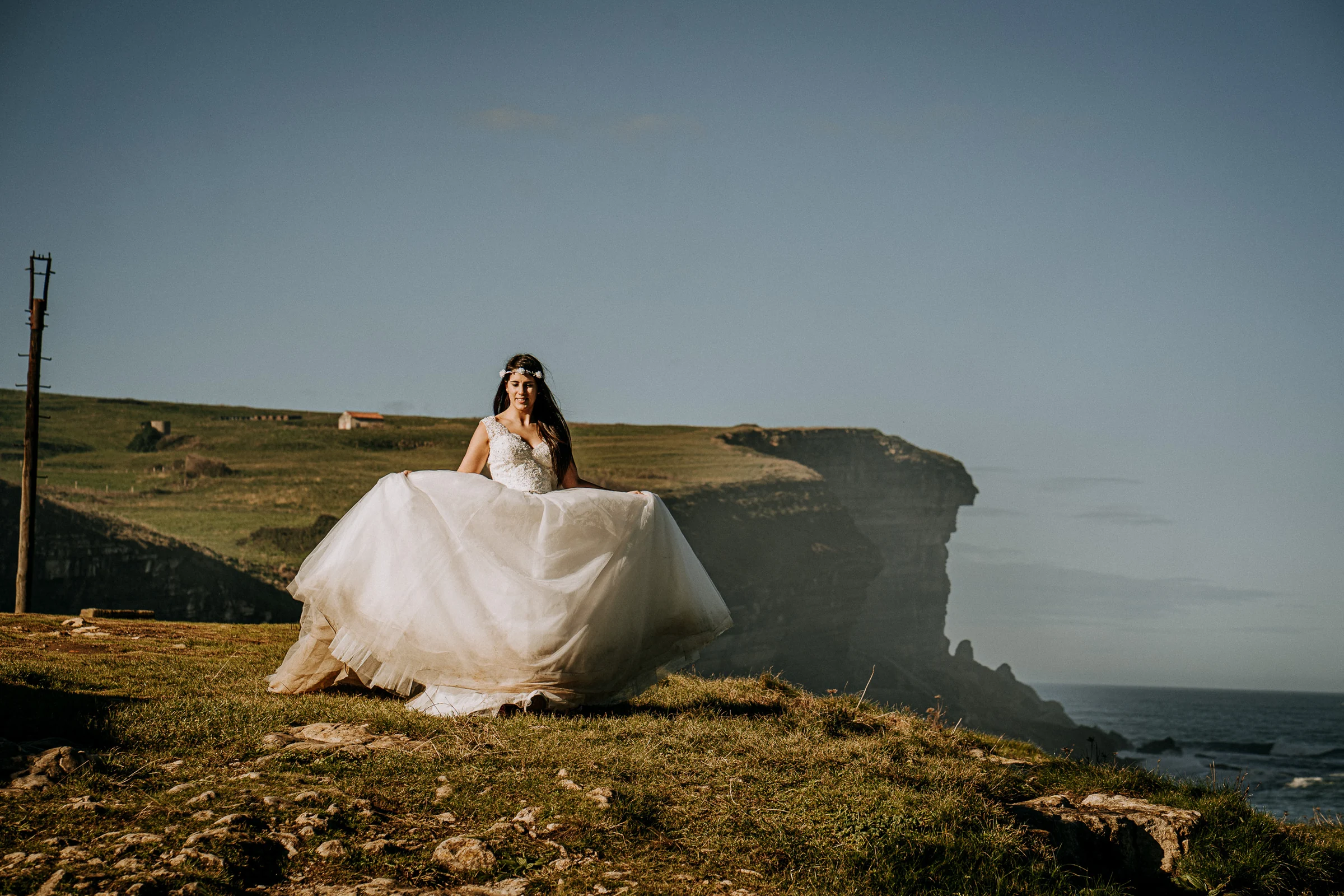 Novia con el vestido extendido ante los acantilados durante una sesión de postboda en El Molino, cerca de Llanes, Asturias.
