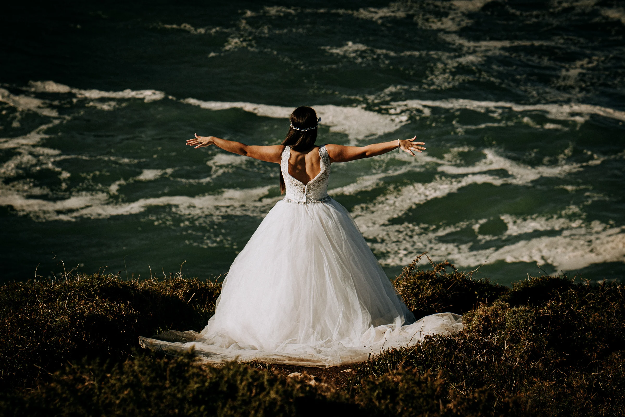 Novia con los brazos abiertos frente al océano durante una sesión de postboda en El Molino, cerca de Llanes, Asturias.