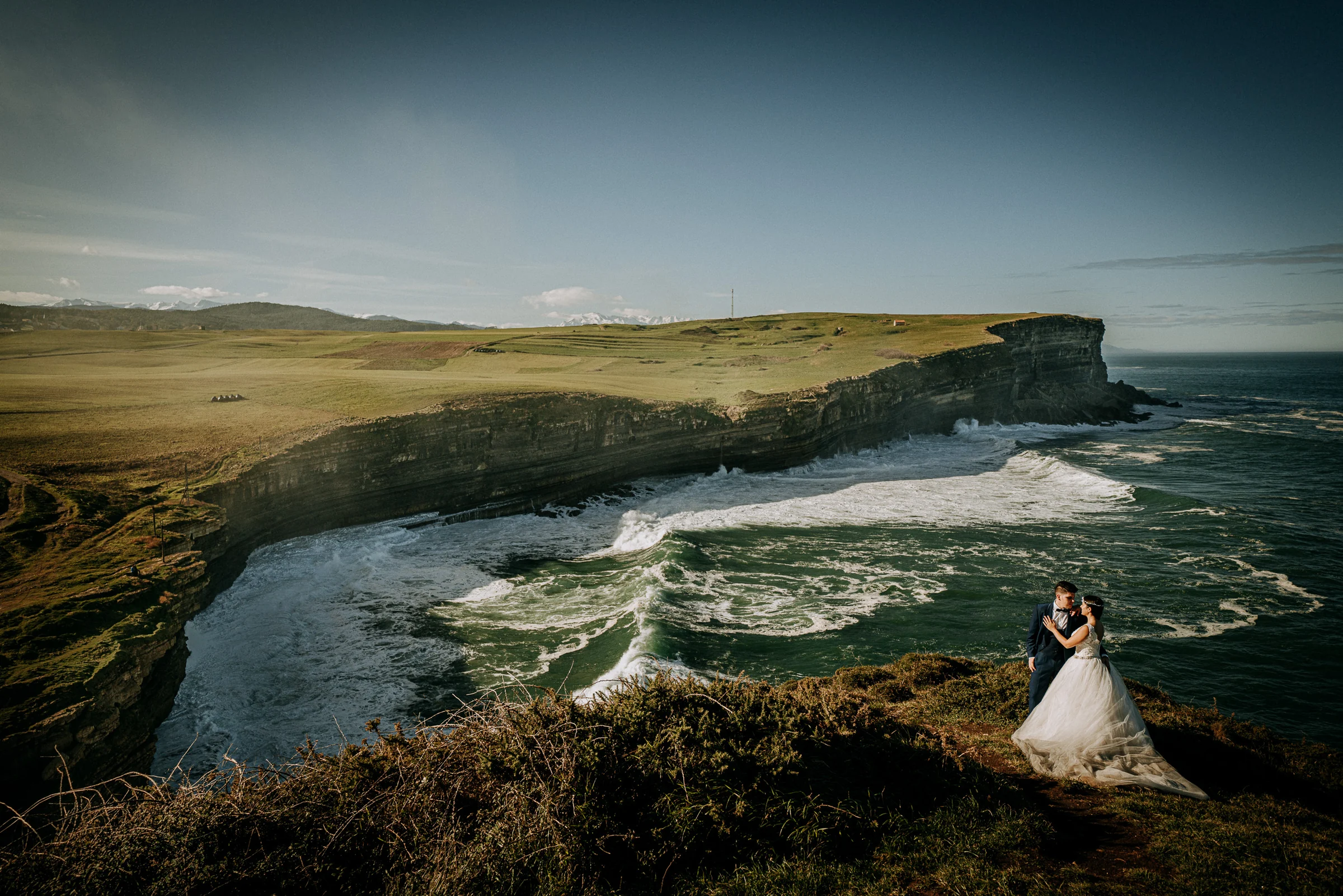 Novia en un gran paisaje de costa y acantilados durante una sesión de postboda en El Molino, cerca de Llanes, Asturias.