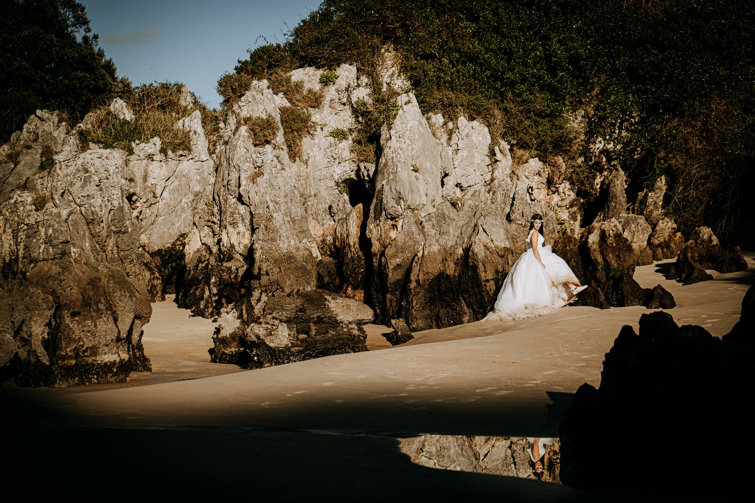 Novia en una playa rodeada de formaciones rocosas durante una sesión de postboda en El Molino, cerca de Llanes, Asturias.