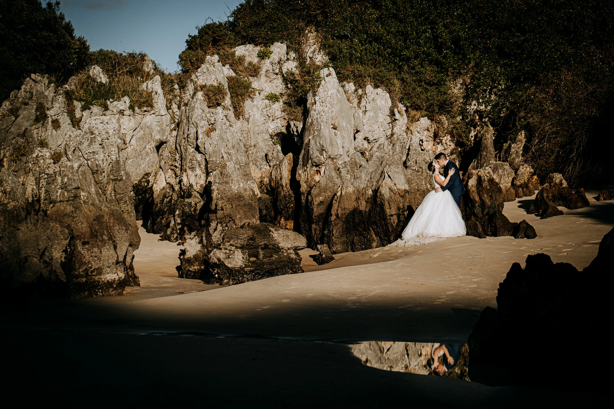 Novia enmarcada por las rocas de una cala durante una sesión de postboda en El Molino, cerca de Llanes, Asturias.