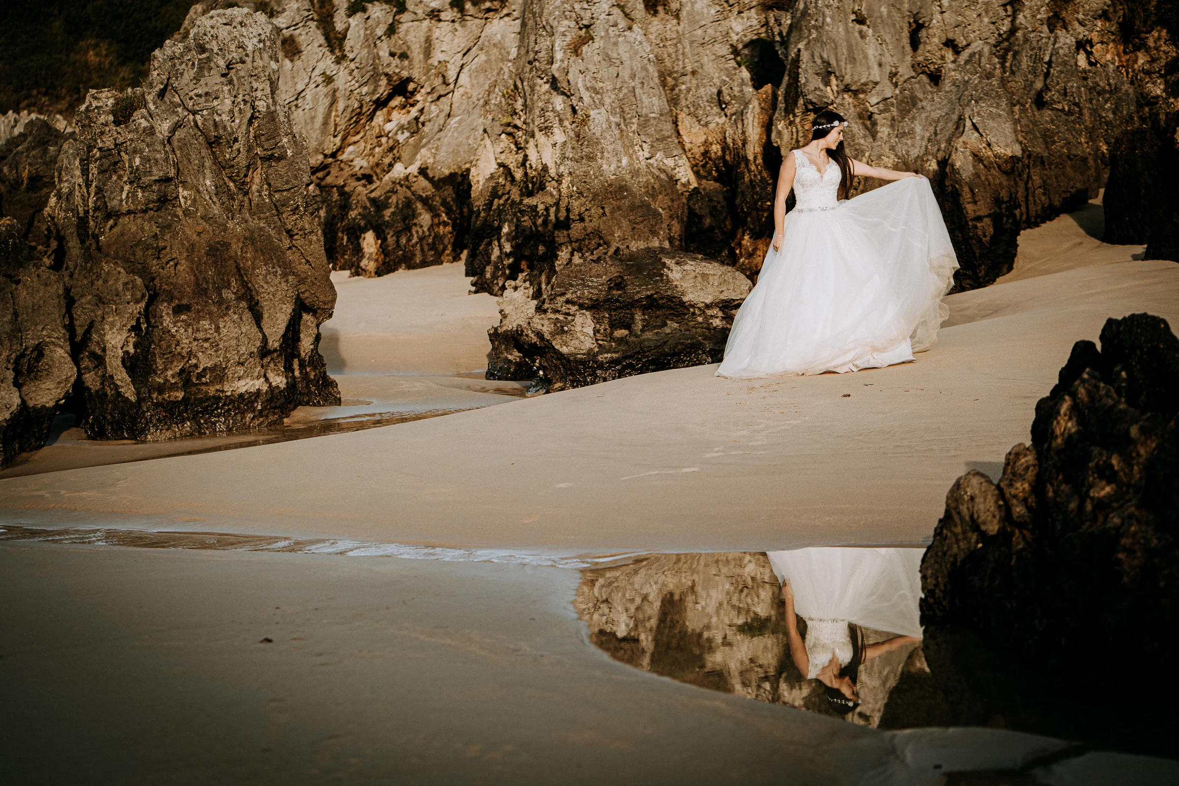 Novia entre formaciones rocosas de una playa salvaje durante una sesión de postboda en El Molino, cerca de Llanes, Asturias.