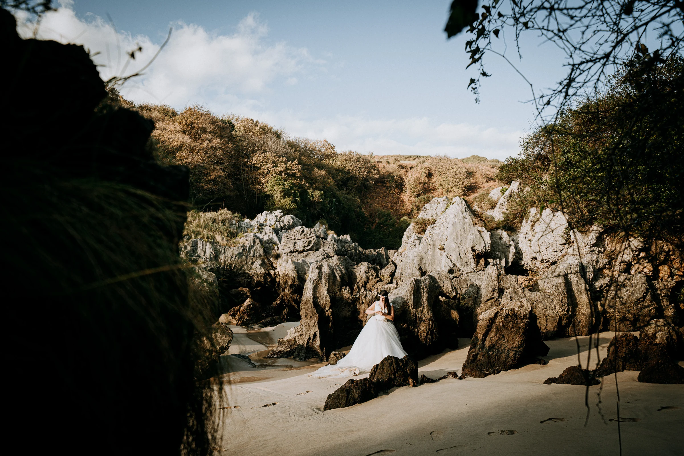 Novia entre grandes rocas de una cala natural durante una sesión de postboda en El Molino, cerca de Llanes, Asturias.