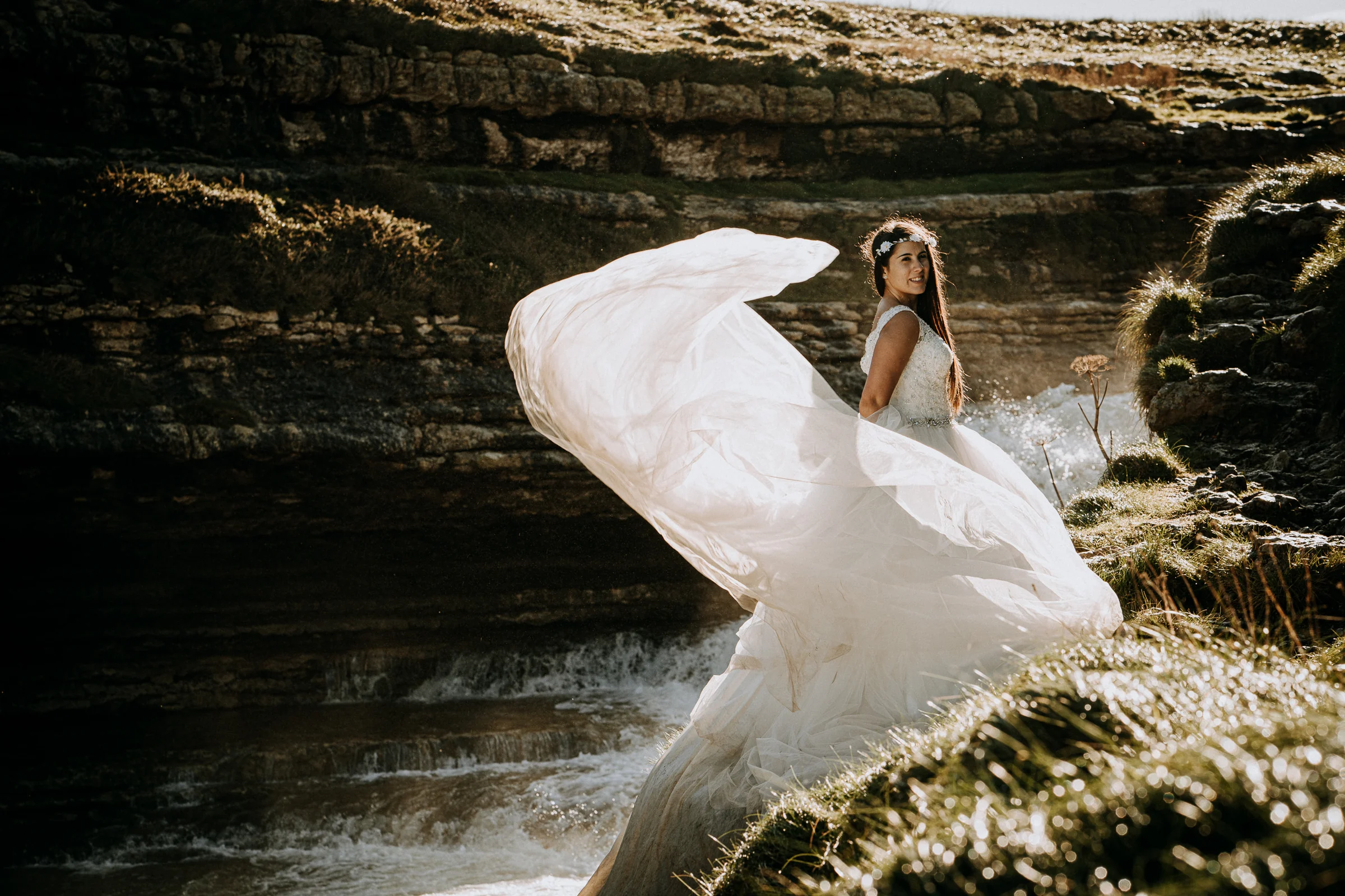 Novia haciendo volar el vestido junto a una cascada durante una sesión de postboda en El Molino, cerca de Llanes, Asturias.