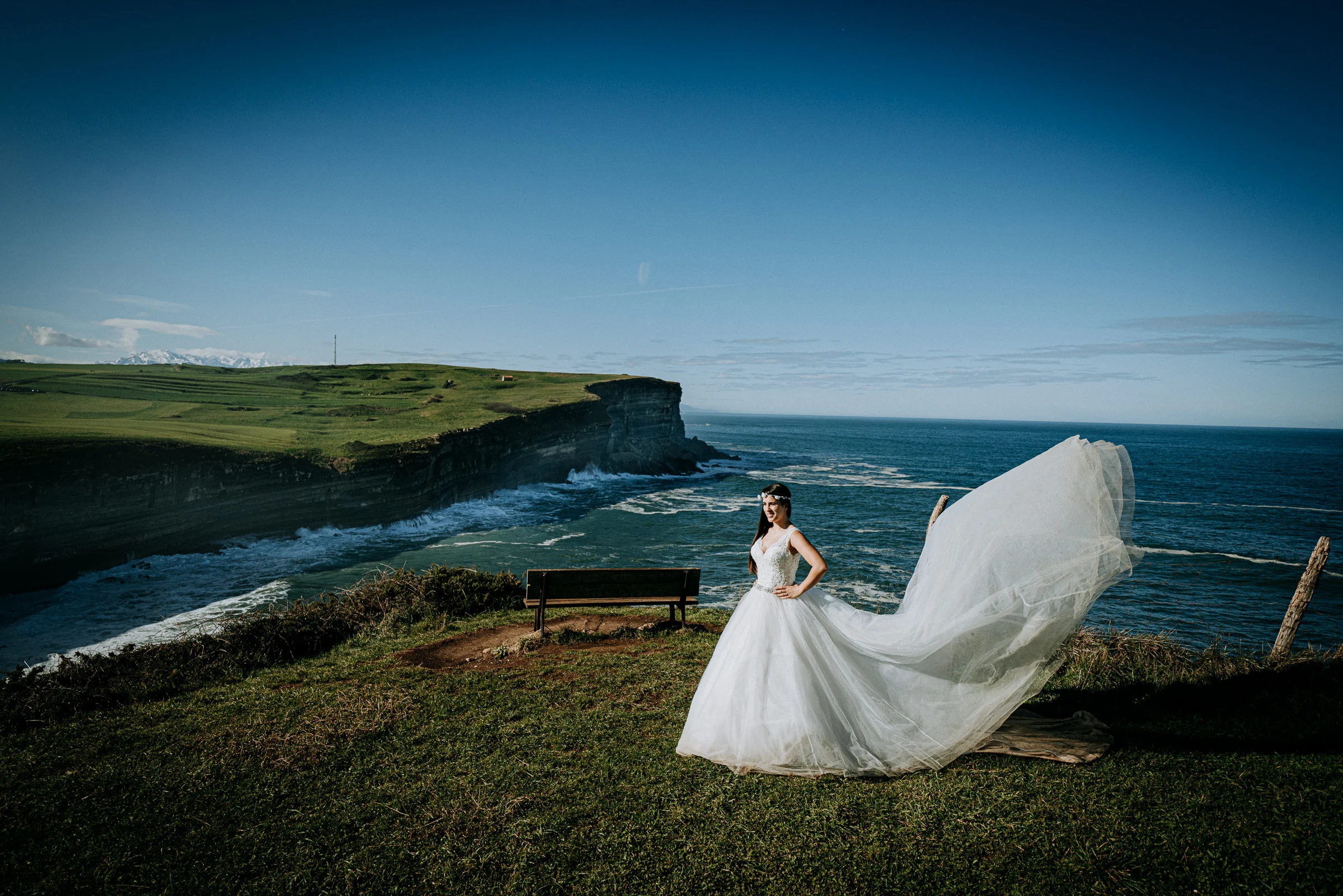 Novia haciendo volar la cola del vestido frente al océano durante una sesión de postboda en El Molino, cerca de Llanes, Asturias.