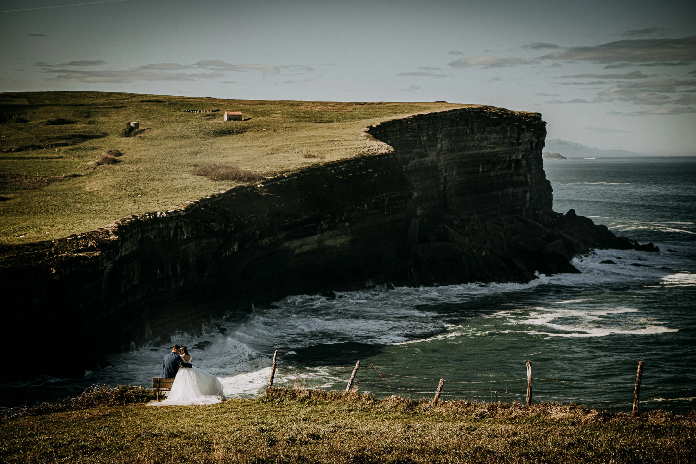 Novia integrada en un gran paisaje de acantilados durante una sesión de postboda en El Molino, cerca de Llanes, Asturias.