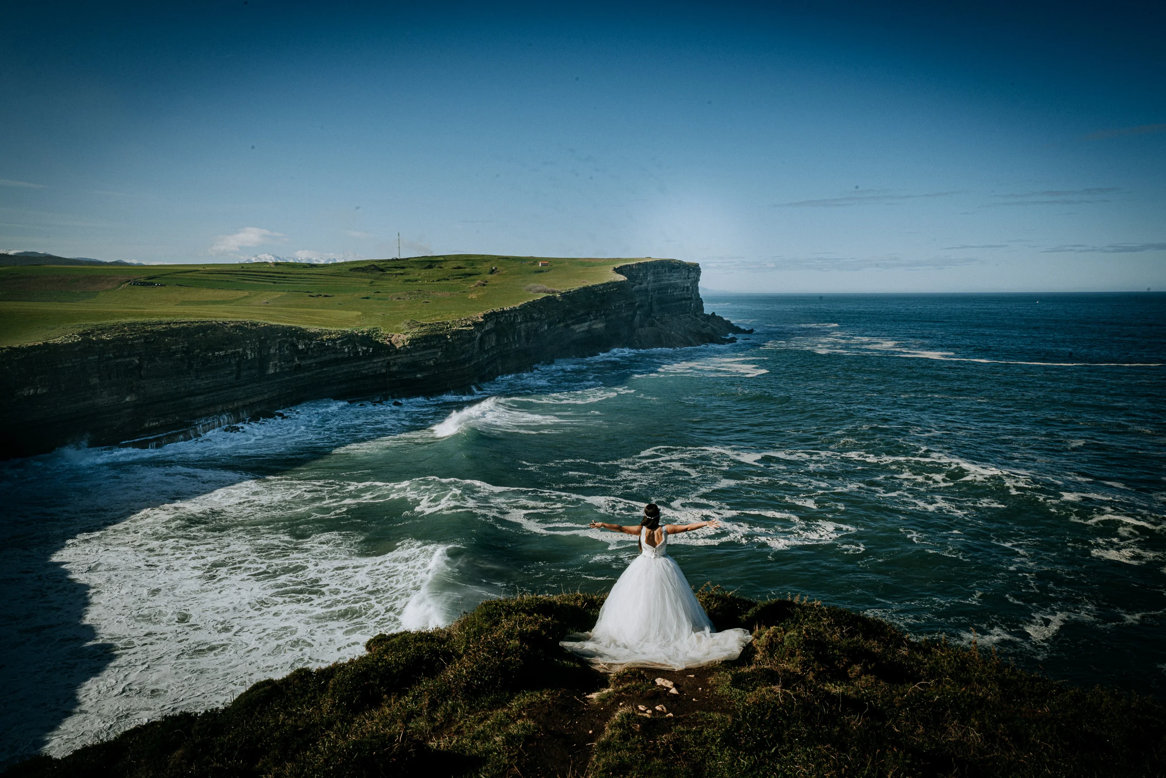 Novia sola mirando al océano desde el acantilado durante una sesión de postboda en El Molino, cerca de Llanes, Asturias.