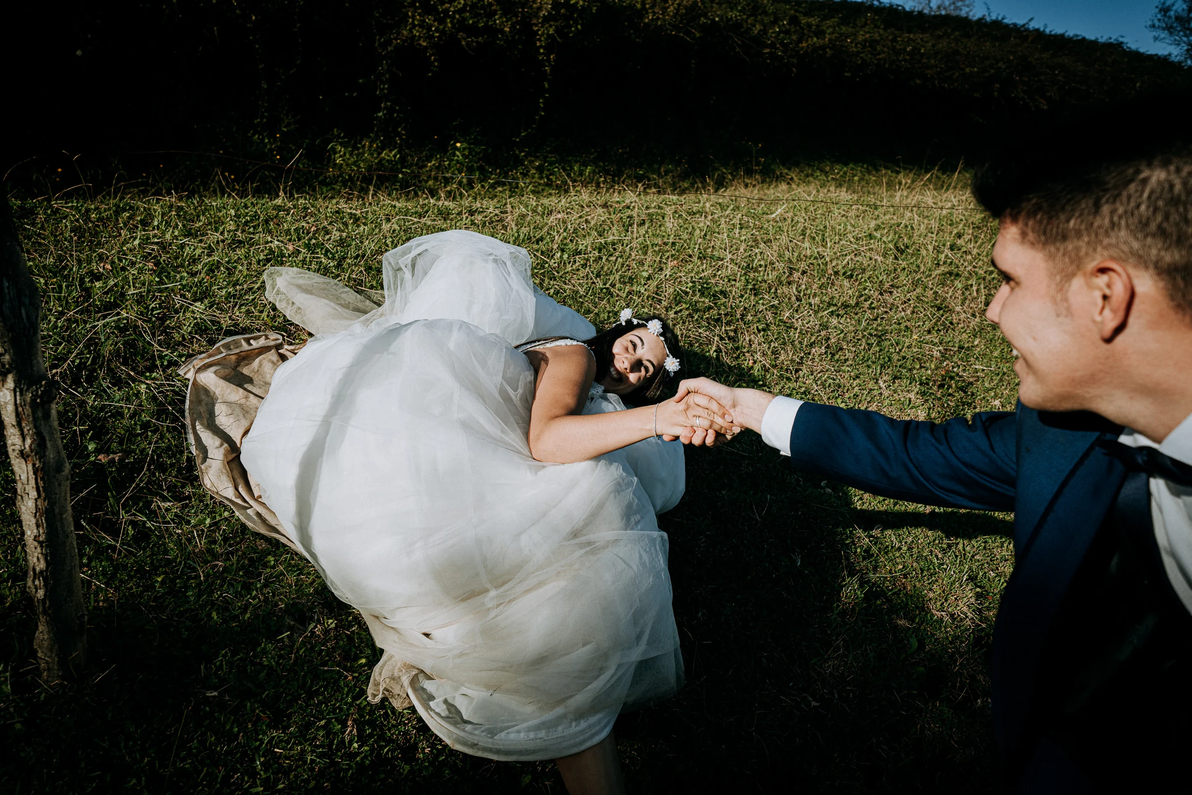 Novia tendida en la hierba cogiendo la mano del novio durante una sesión de postboda en El Molino, cerca de Llanes, Asturias.