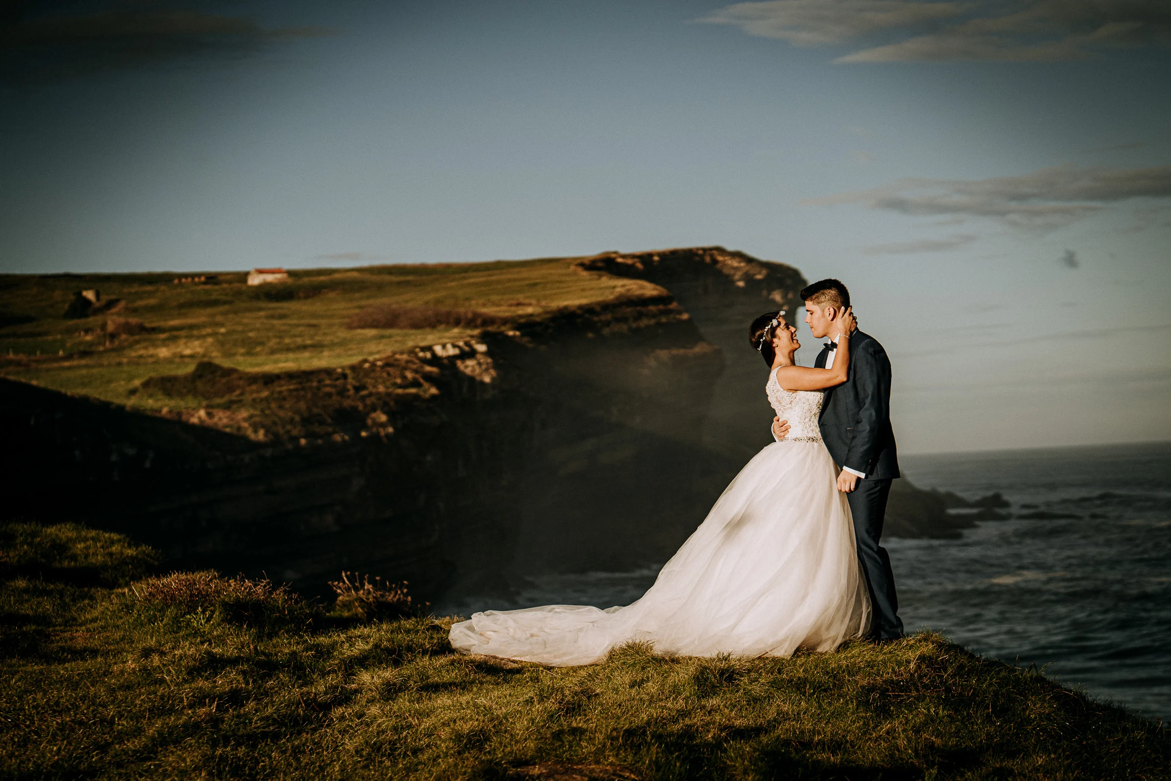 Pareja abrazada al borde del acantilado al final del día durante una sesión de postboda en El Molino, cerca de Llanes, Asturias.
