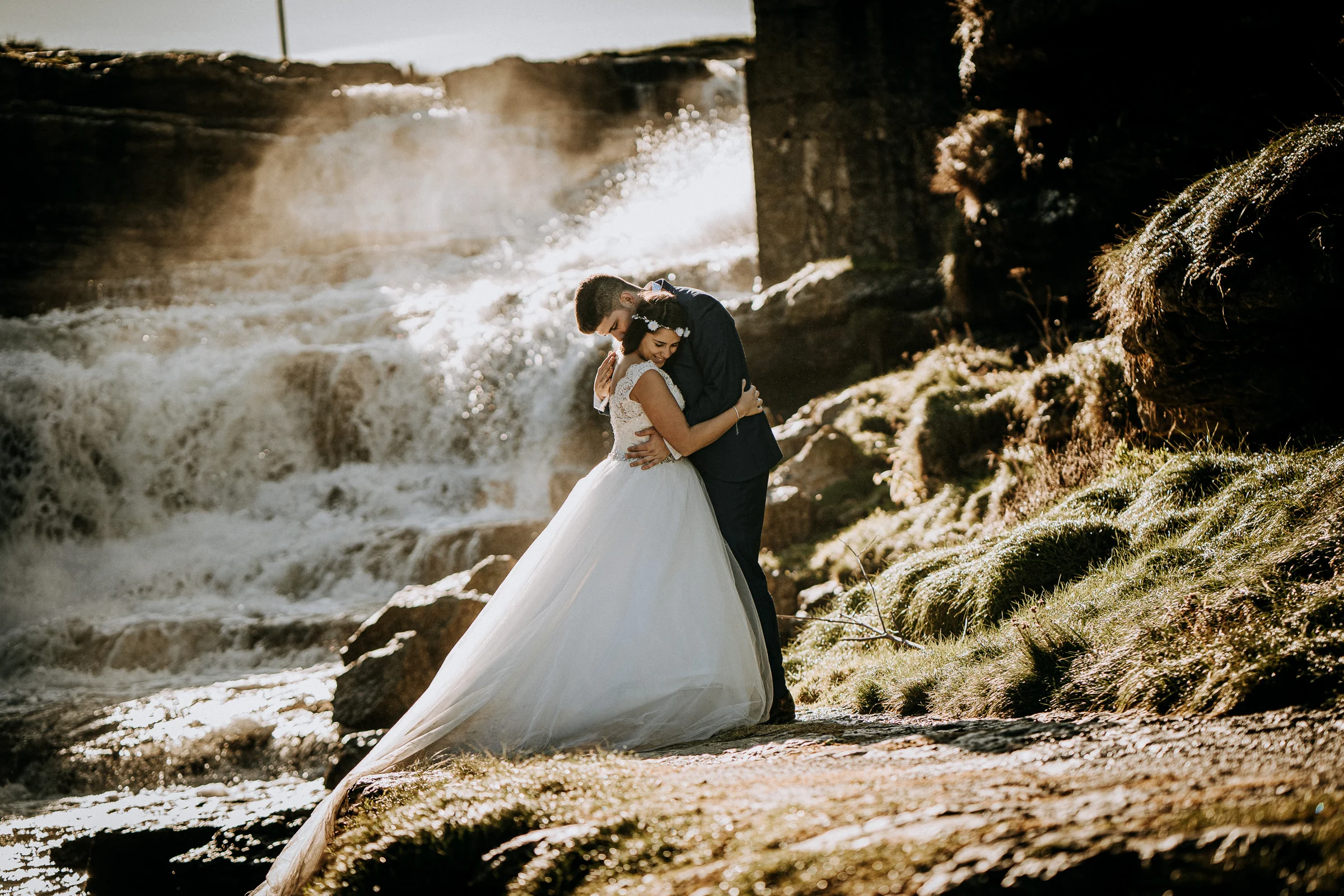Pareja abrazada con luz dorada y cascada al fondo durante una sesión de postboda en El Molino, cerca de Llanes, Asturias.
