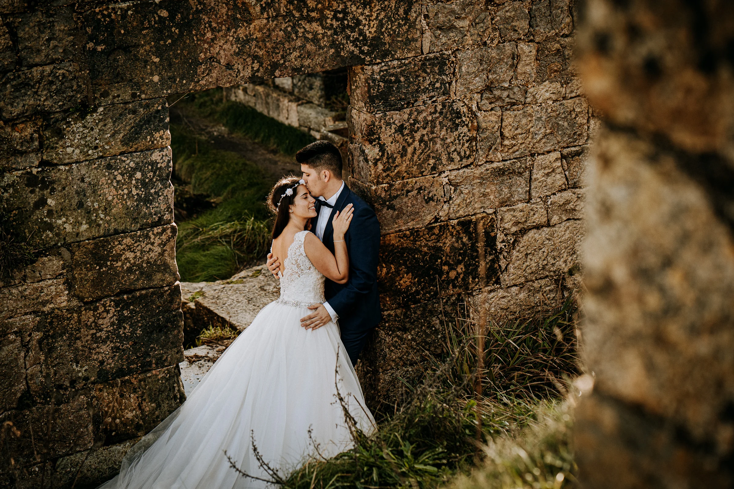 Pareja abrazada en la entrada de unas ruinas durante una sesión de postboda en El Molino, cerca de Llanes, Asturias.