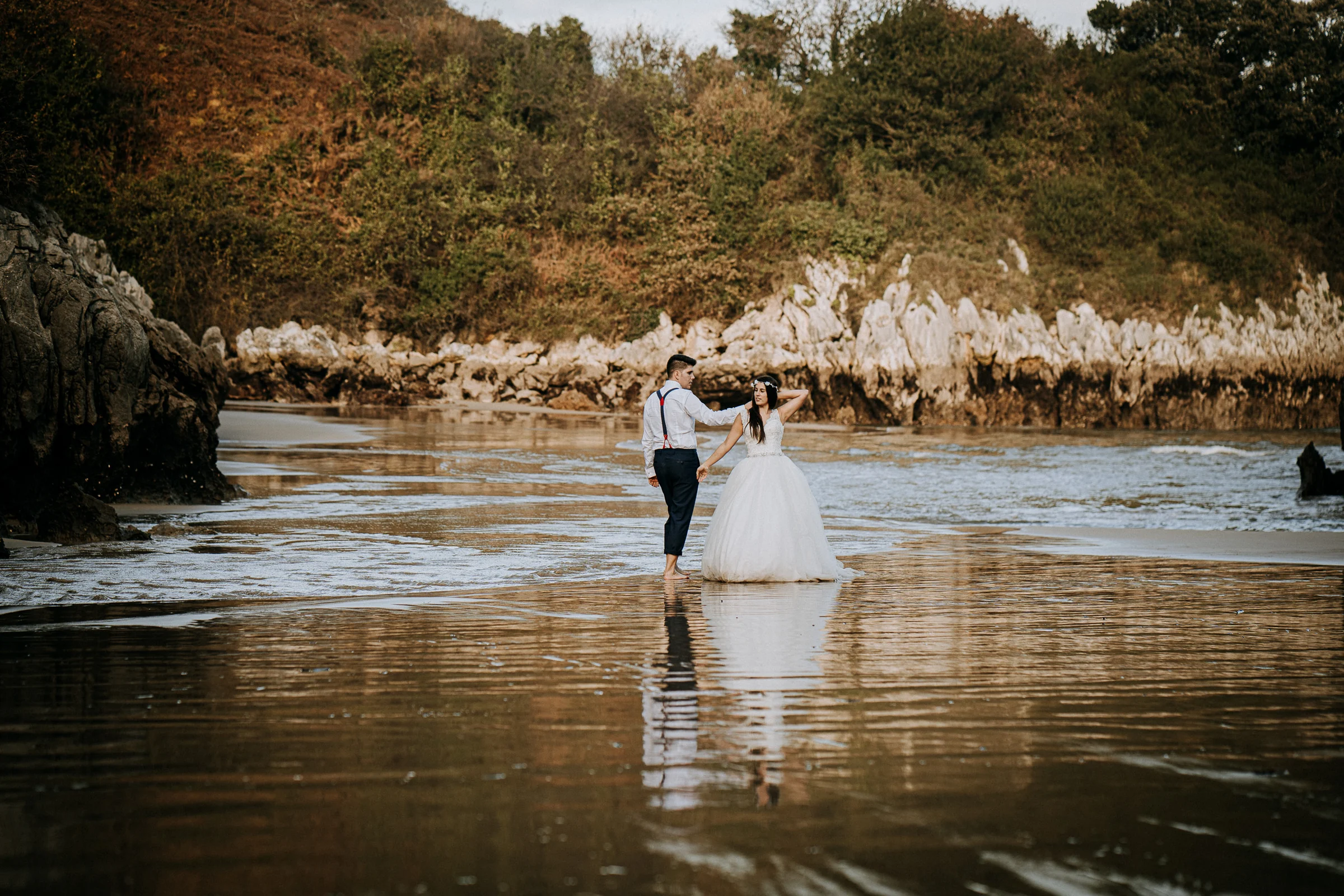 Pareja abrazada en la playa con rocas al fondo durante una sesión de postboda en El Molino, cerca de Llanes, Asturias.